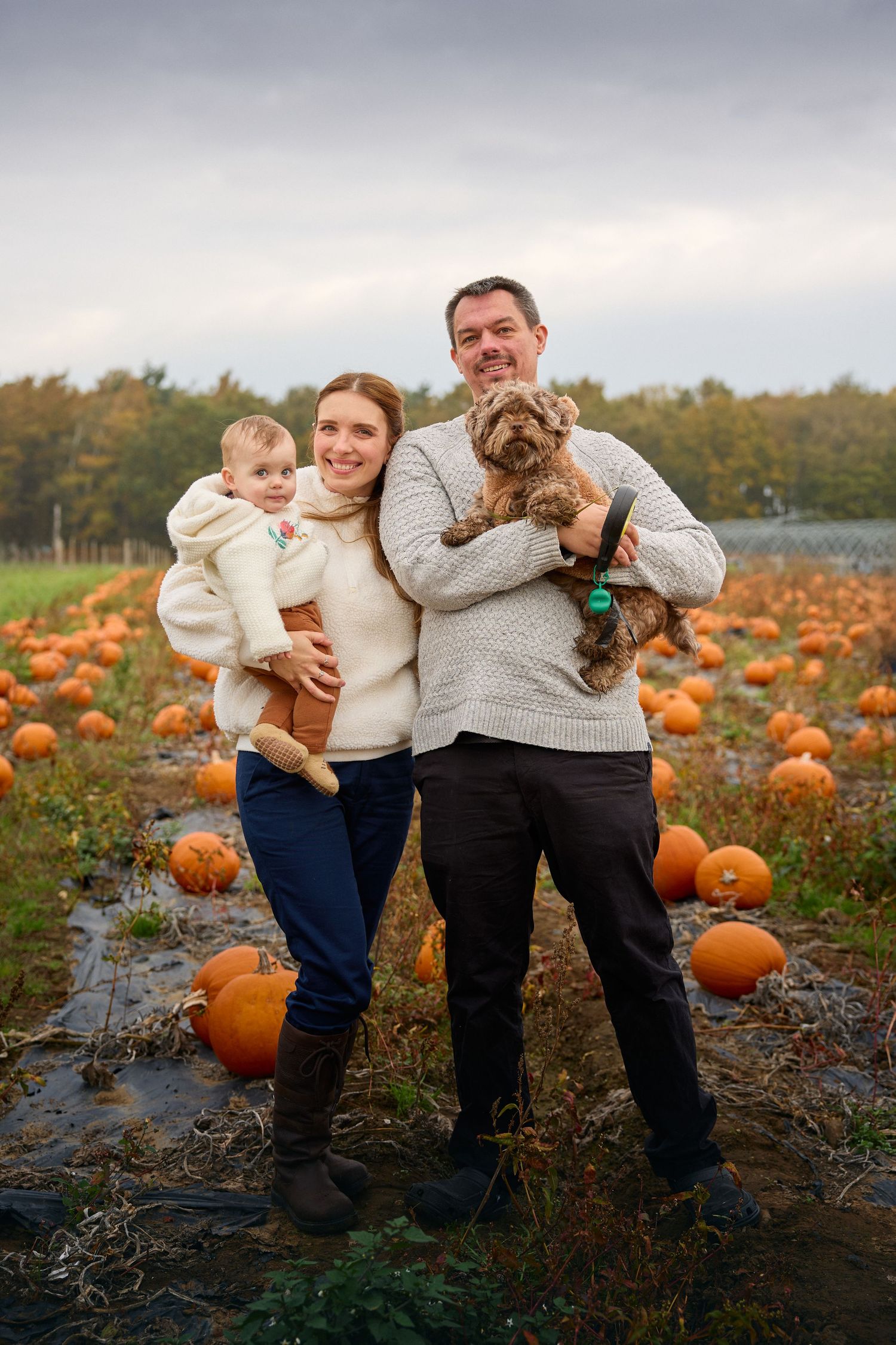 A family poses with their dog in a pumpkin patch during autumn.