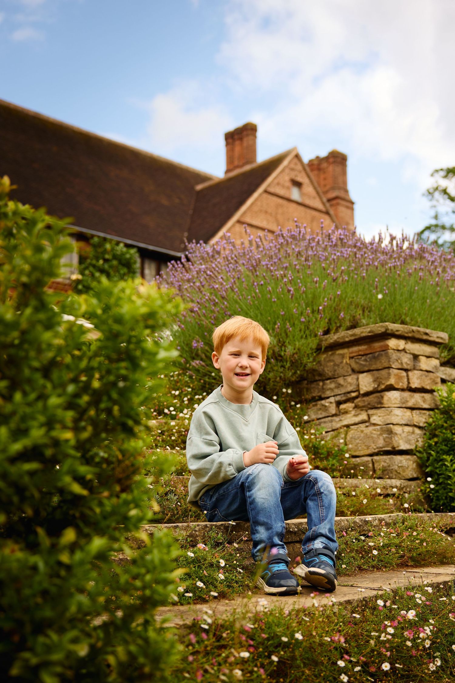 Child relaxing on stone garden steps surrounded by lavender and daisies.