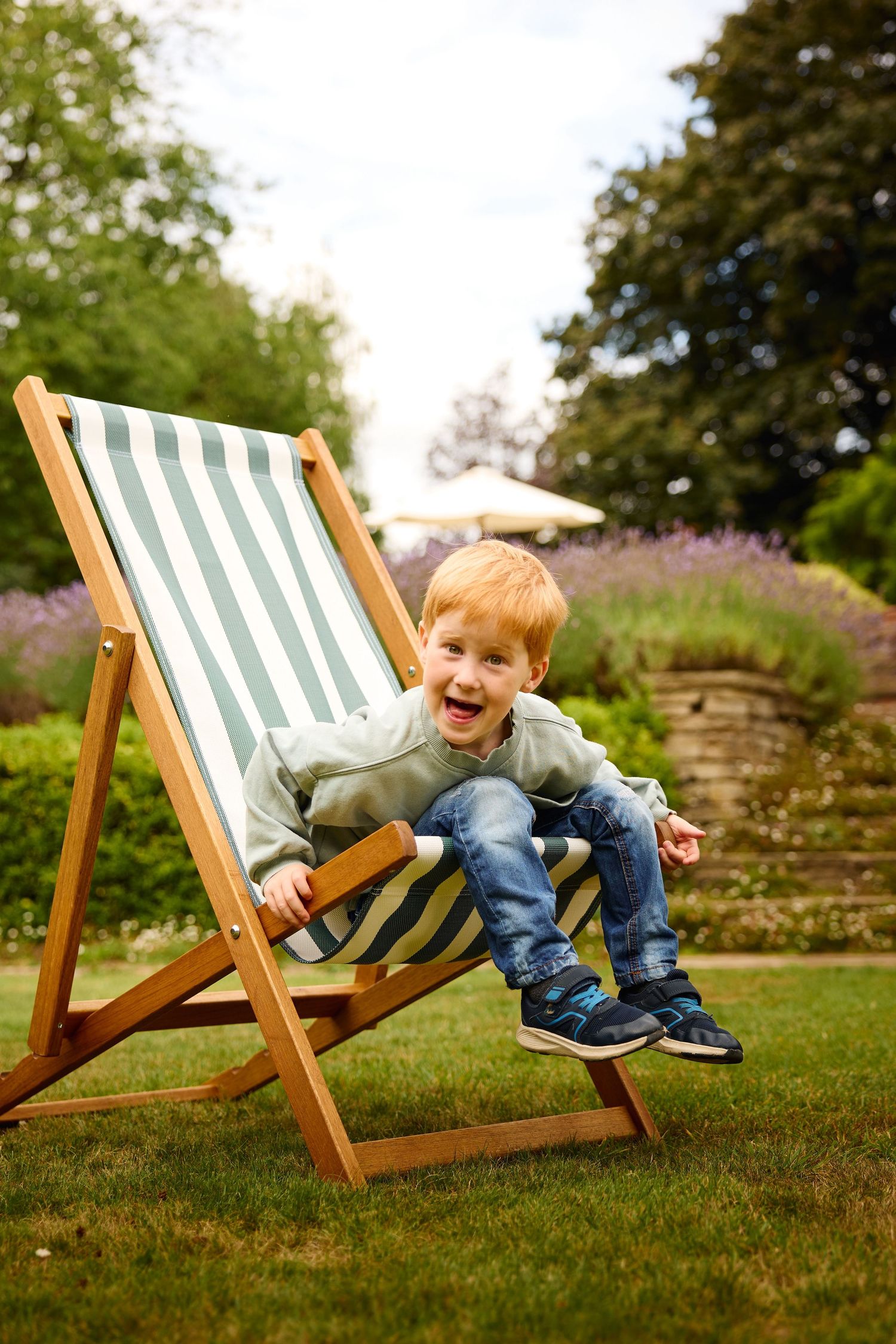 Child playing and laughing on striped deck chair in garden setting.