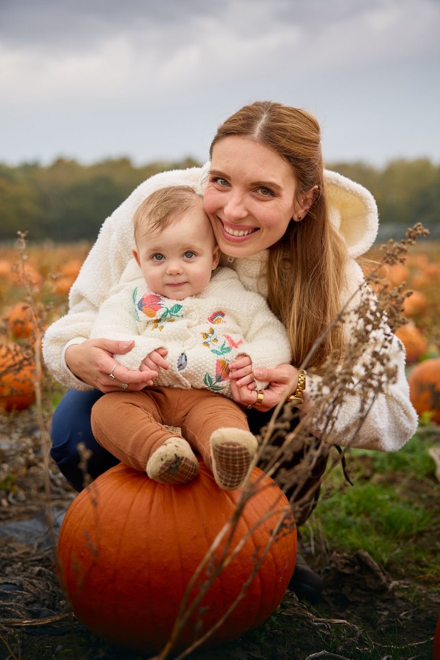 Autumn scene with people sitting on large orange pumpkin in field at sunset.