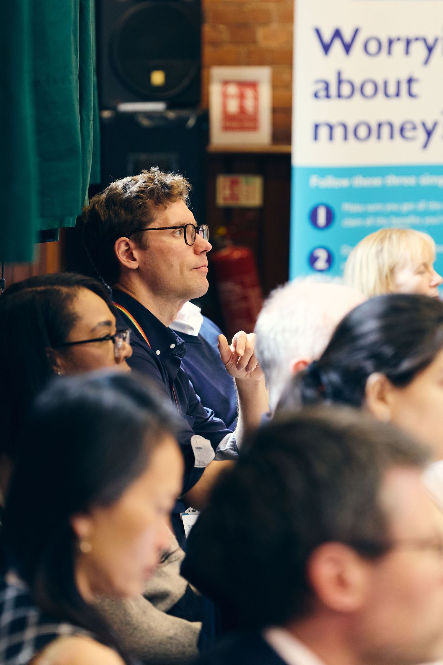 Audience members attentively listening at a financial seminar with a 'Worry About Money' banner in the background.