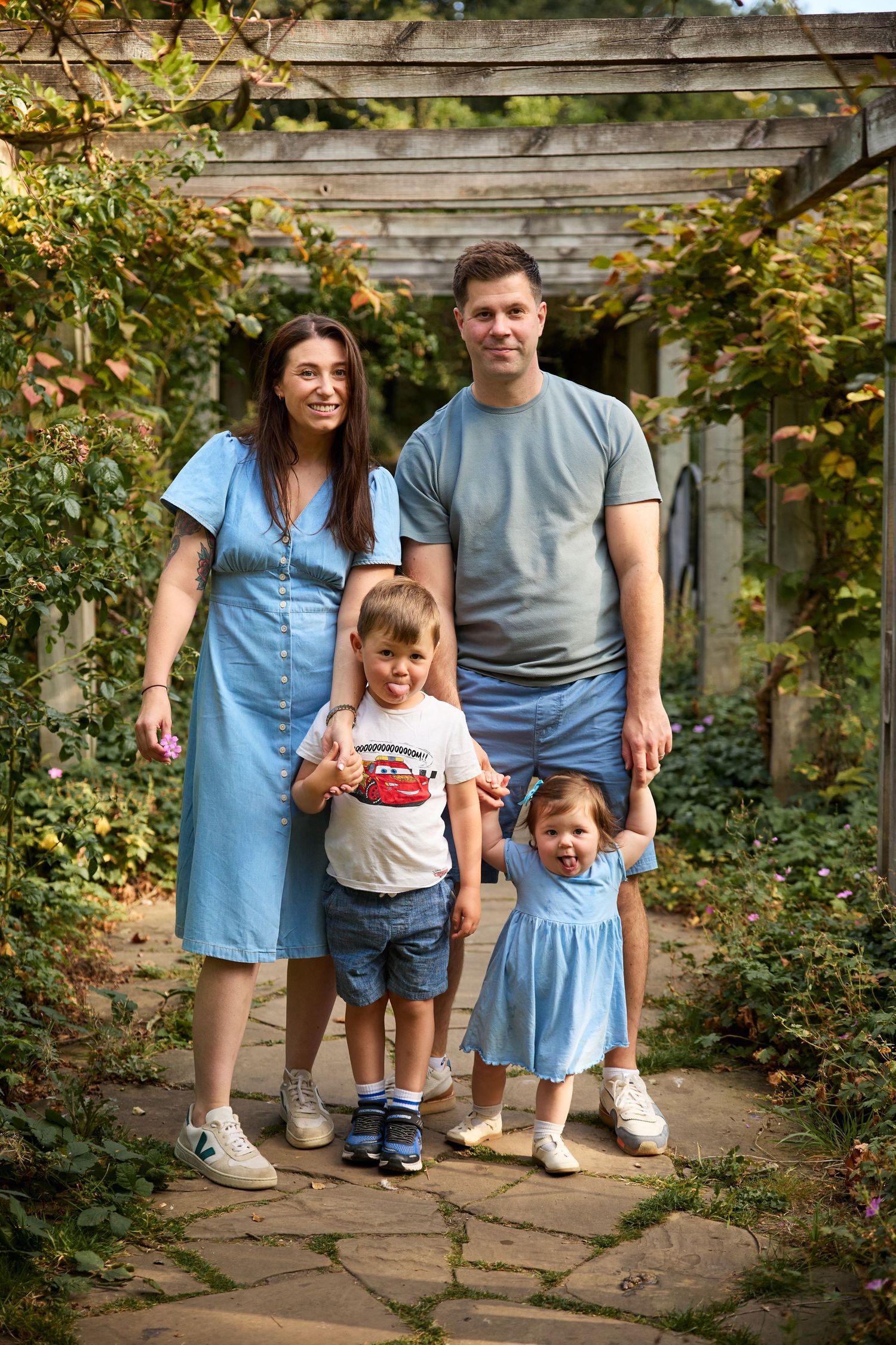 Family group poses together under a vine-covered garden pergola on stone path.