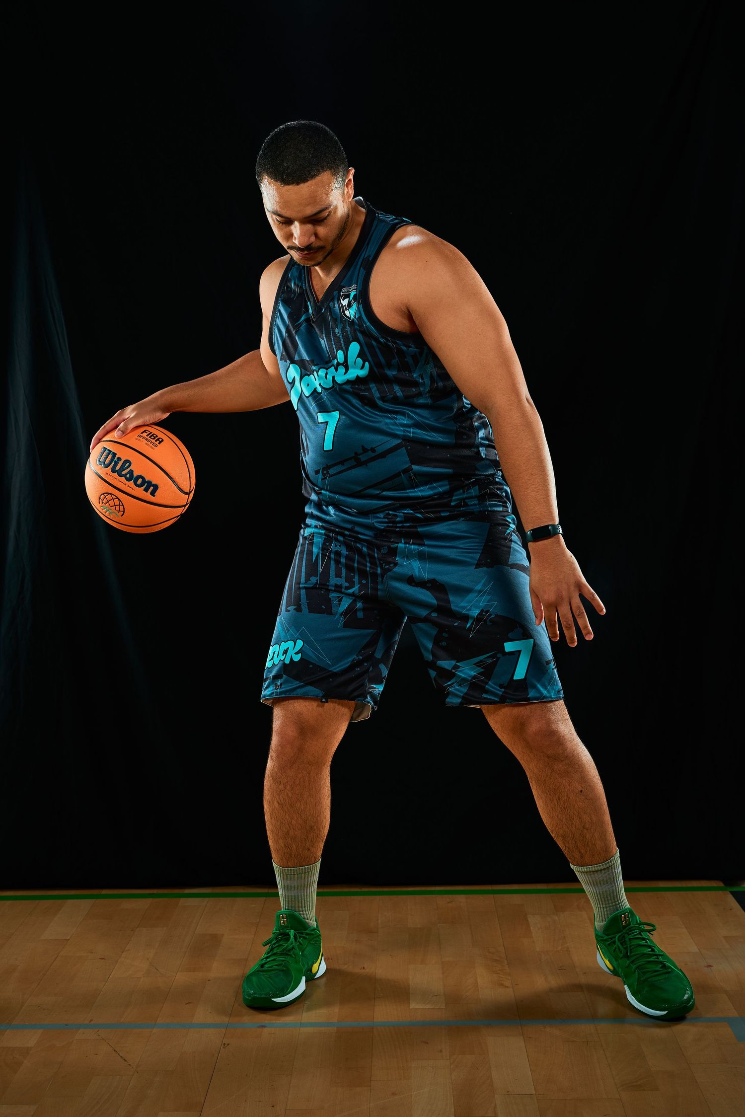 Basketball player in navy uniform demonstrating low dribbling technique on wooden court.