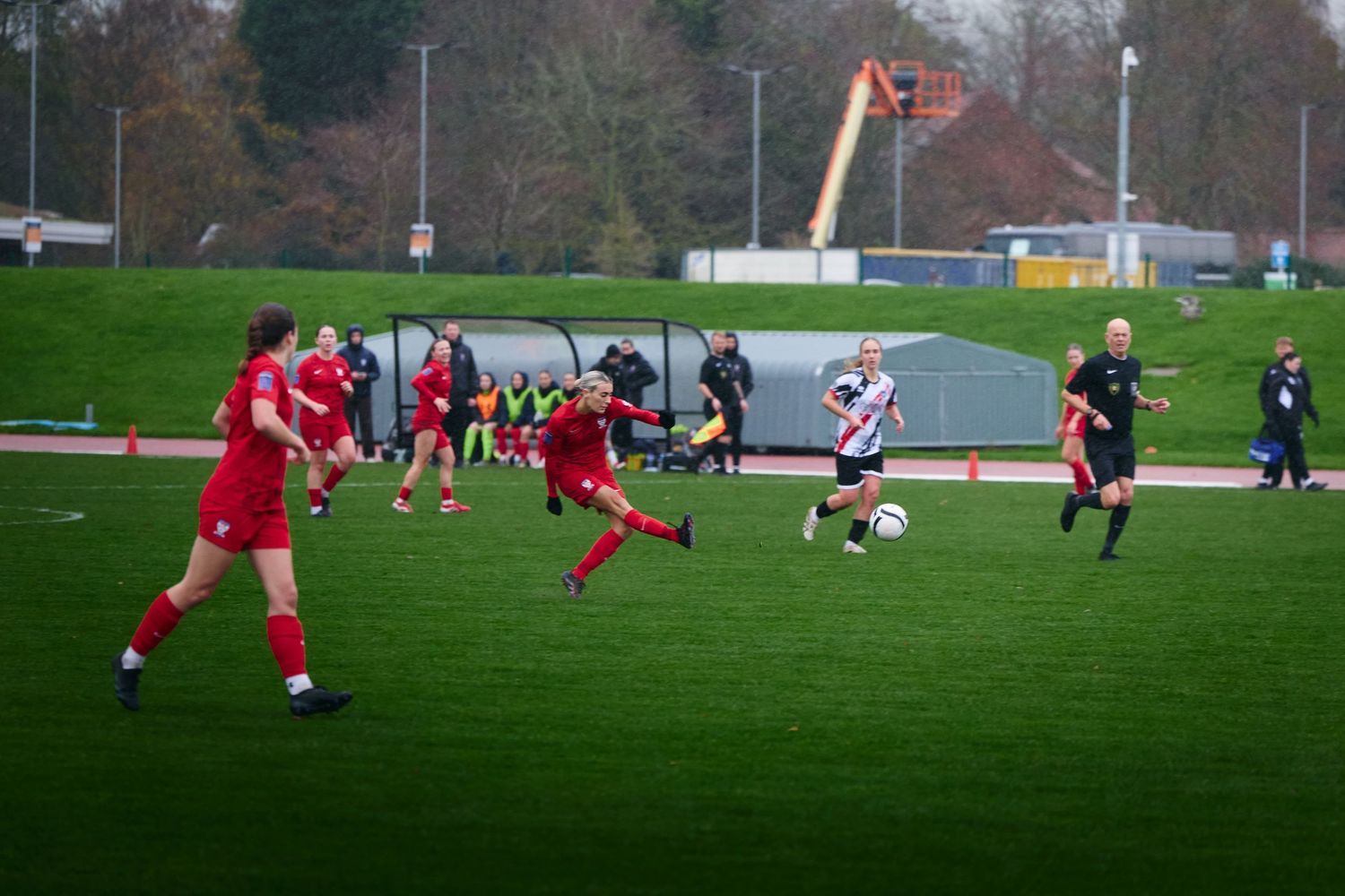 Soccer players in red and black uniforms compete for the ball on a green grass field during a match.