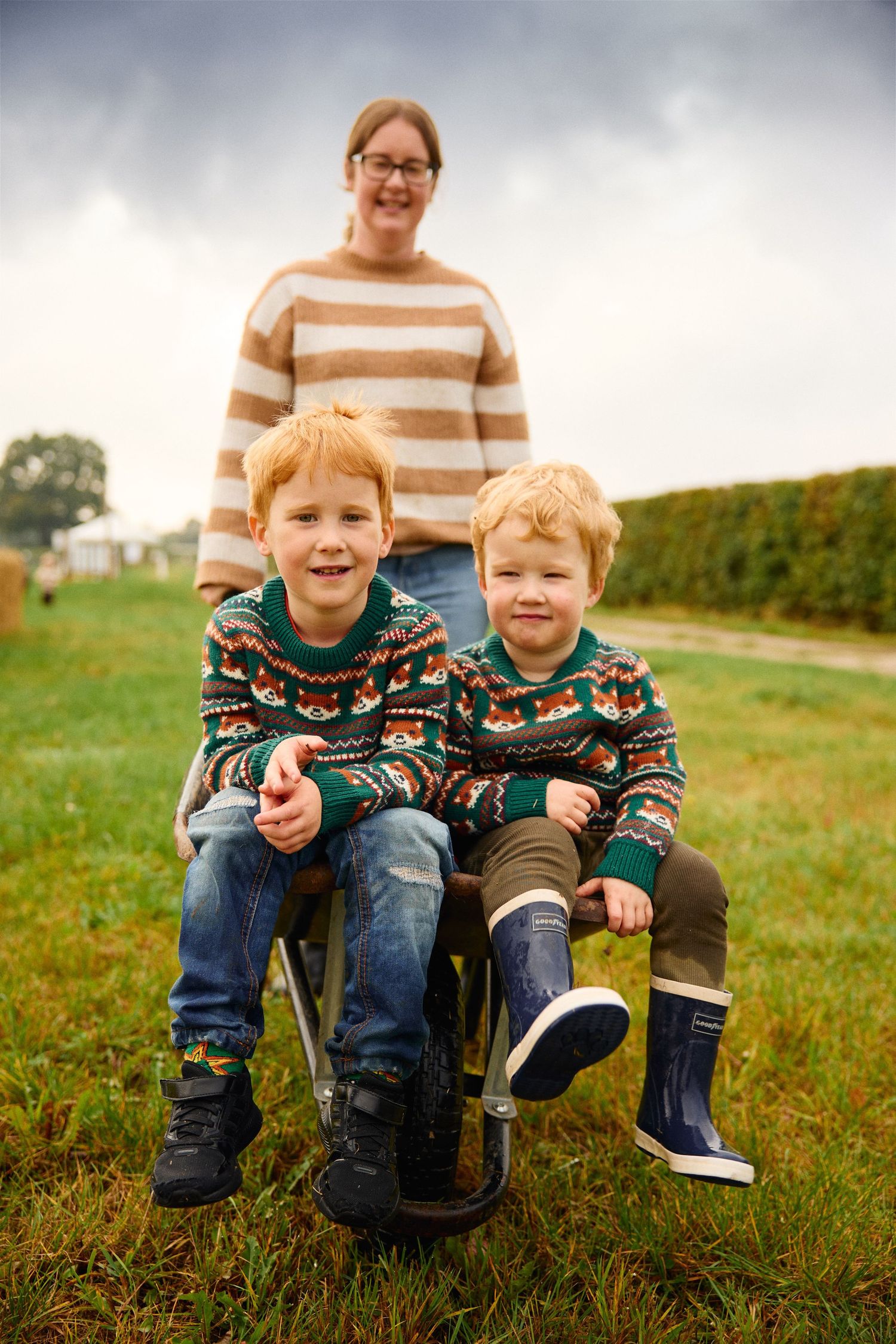 Children in matching sweaters sit together on grassy hill during fall season.