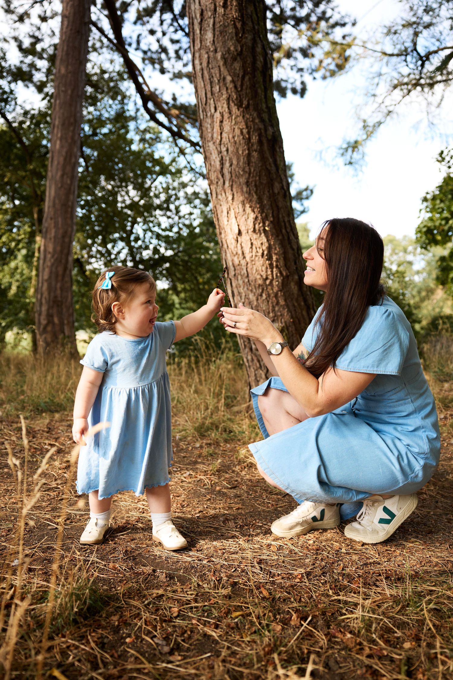 Parent and child sit together on pine needles under tall trees during an outdoor photo session.