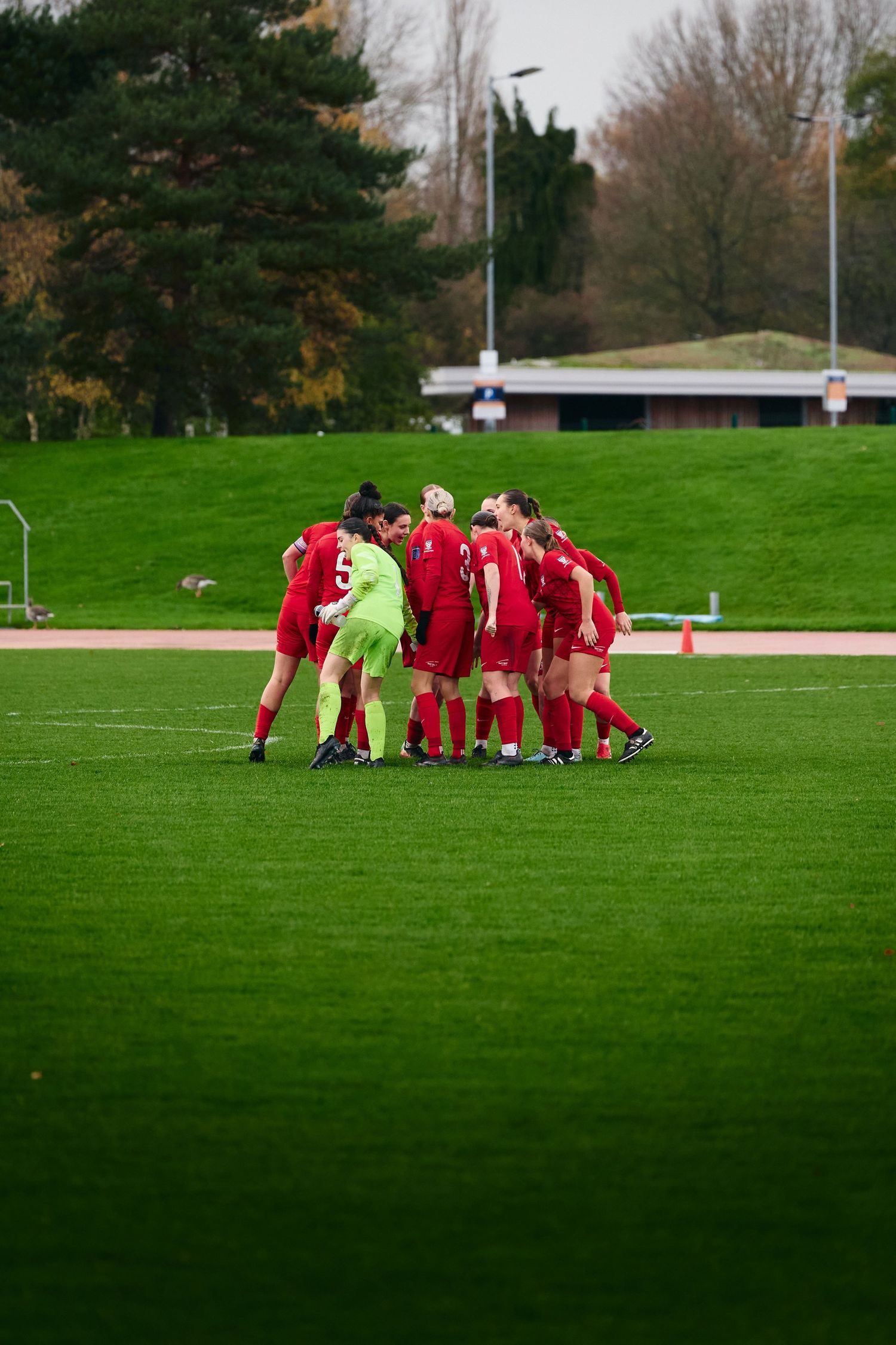 A soccer team huddles together in a tight circle on a green grass field during a match or practice session.