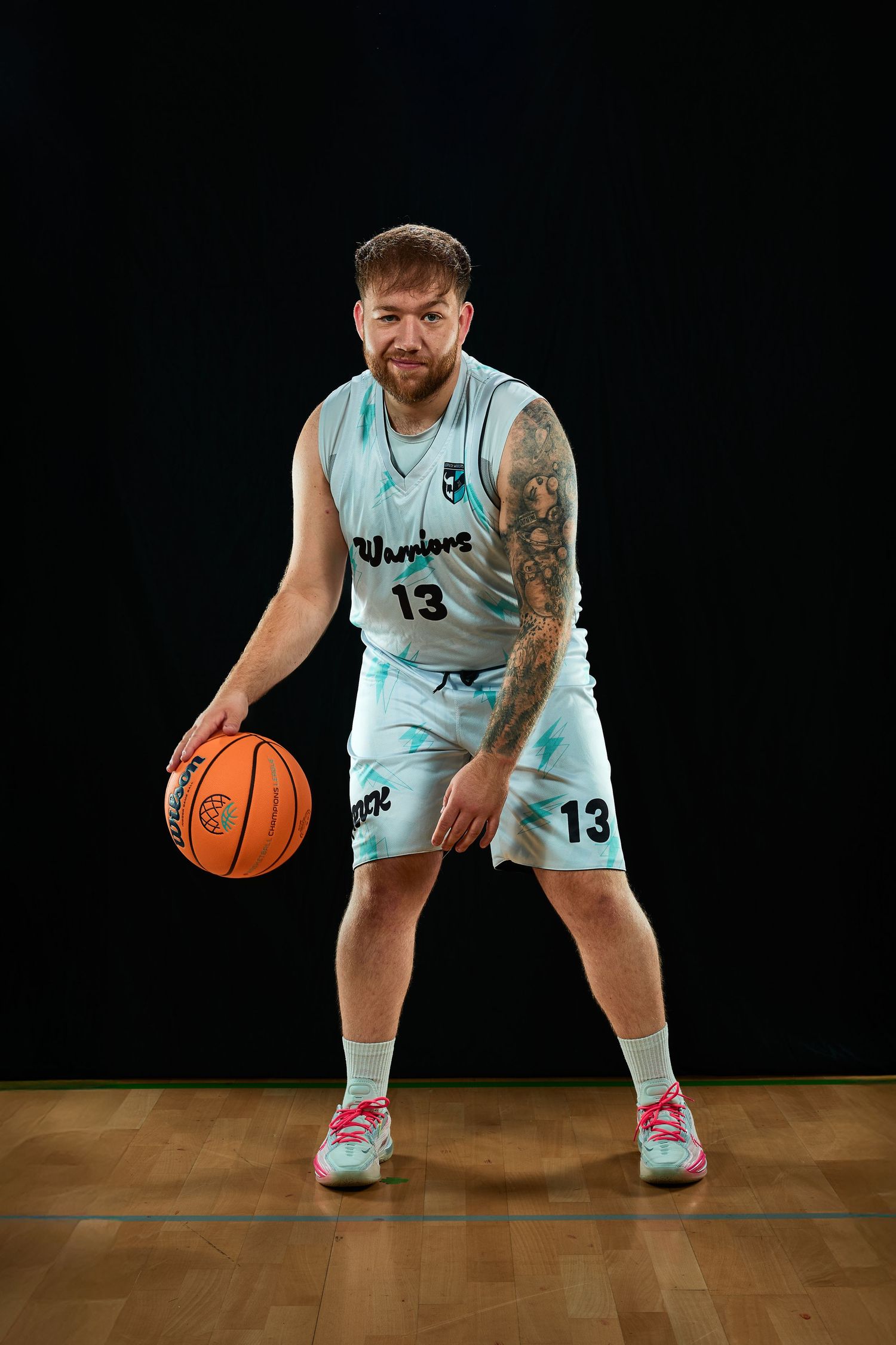 Basketball player in light blue jersey number 13 dribbling low on wooden court.