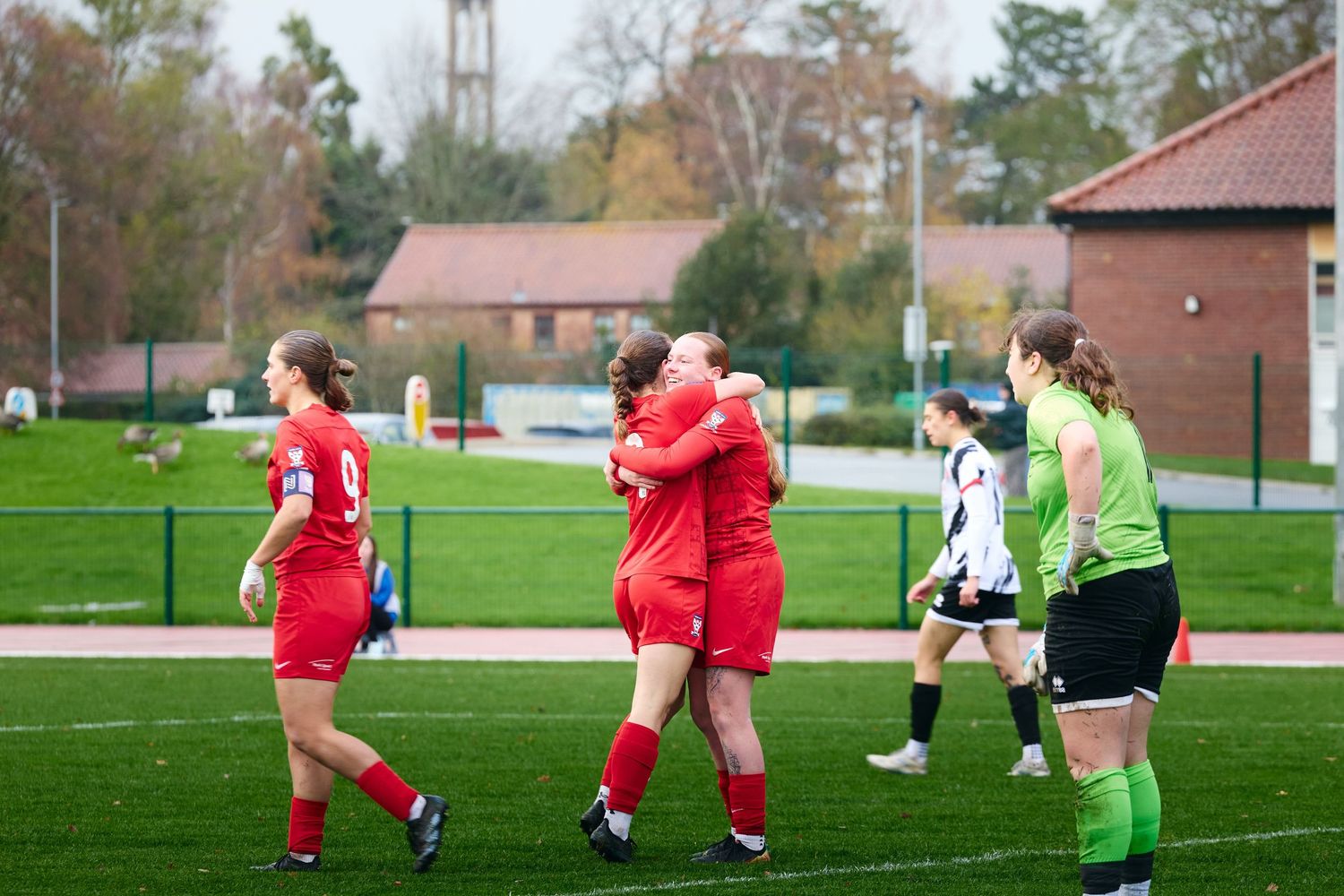 Soccer players in red uniforms celebrate on a green turf field during a match while opponents look on.