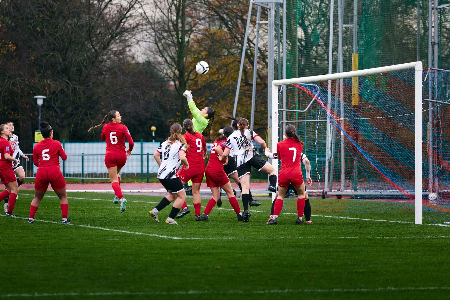 Soccer players in red and white uniforms compete for the ball during an intense match on a grass field.