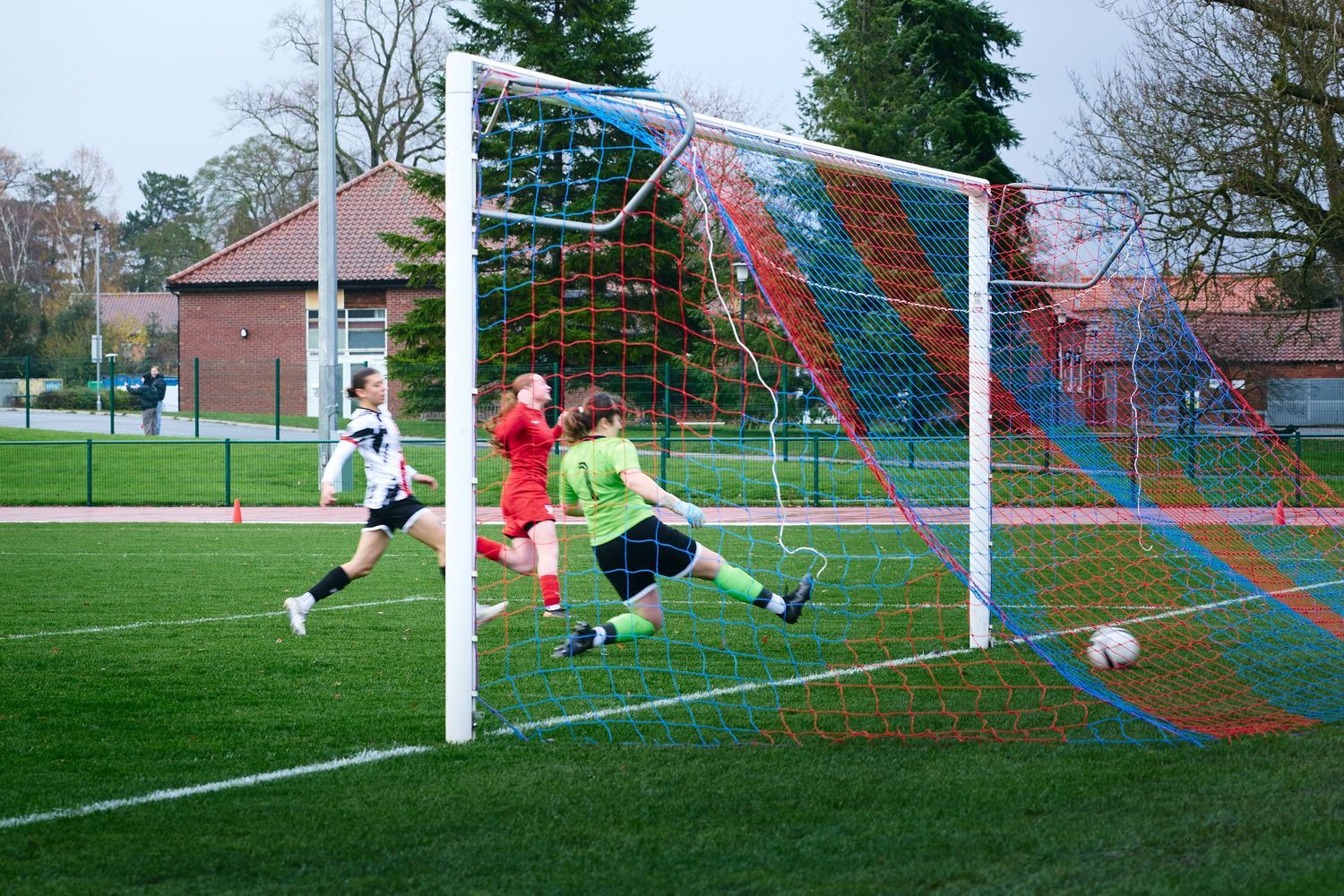 A sequence of soccer action shots shows a diving save attempt at a goal on a grass field during a match.