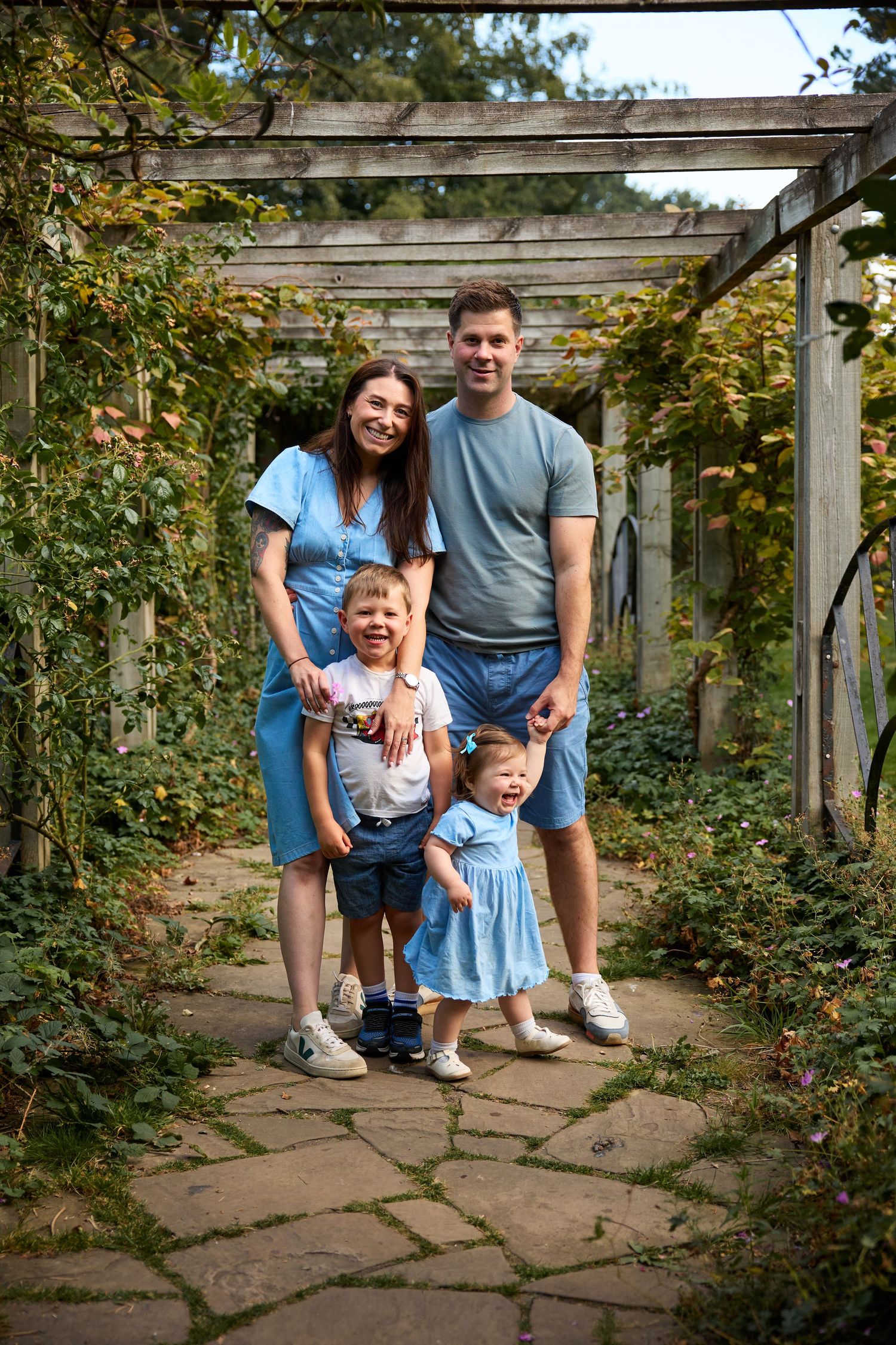 Family shares joyful moment together under wooden garden arbor with climbing vines.