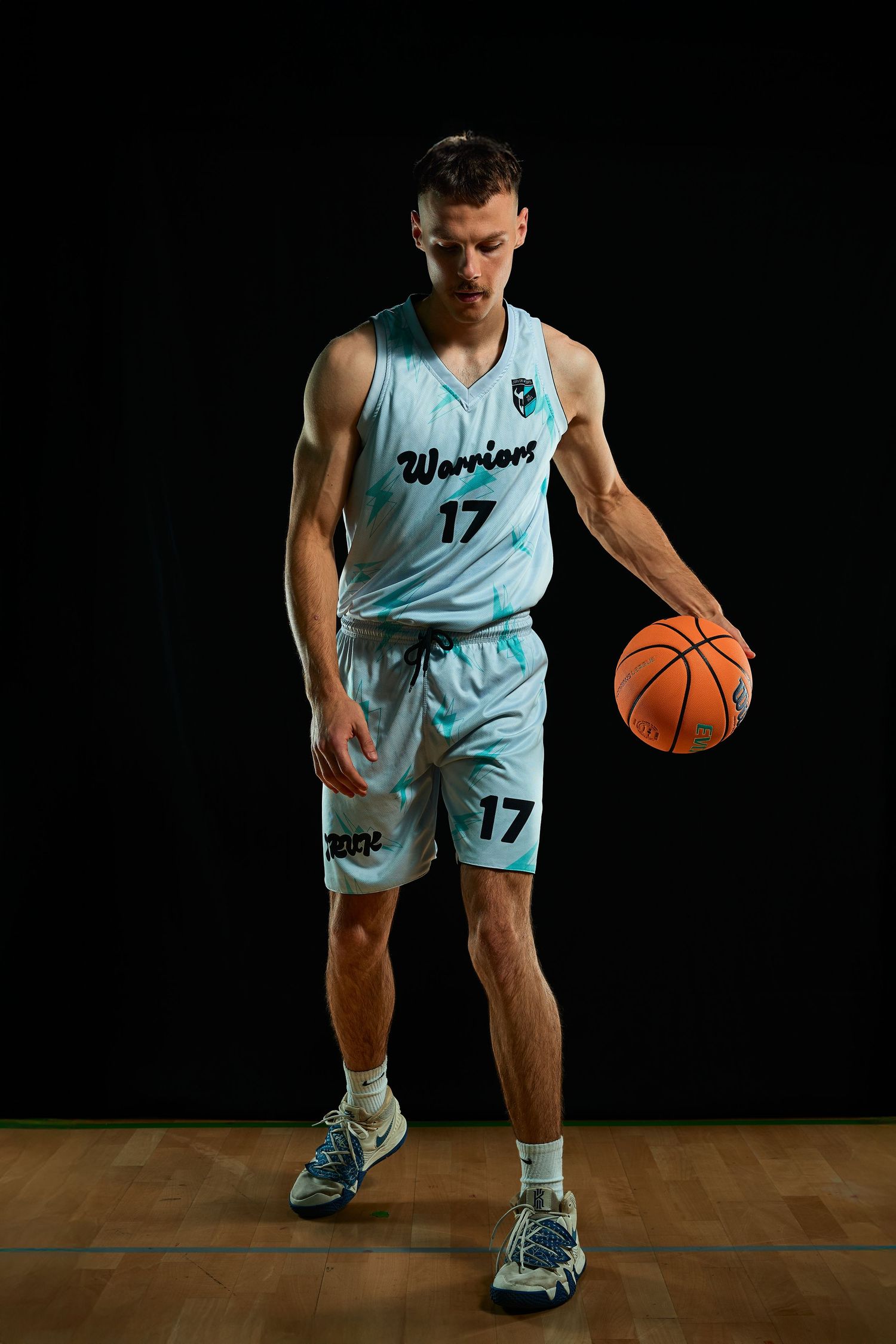 Basketball player in light blue uniform dribbles ball on wooden court.