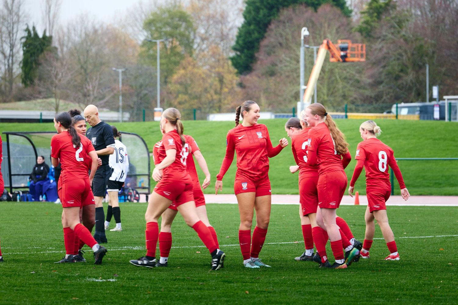 Soccer players in red uniforms stretch on a grass field during a pre-game warmup session.