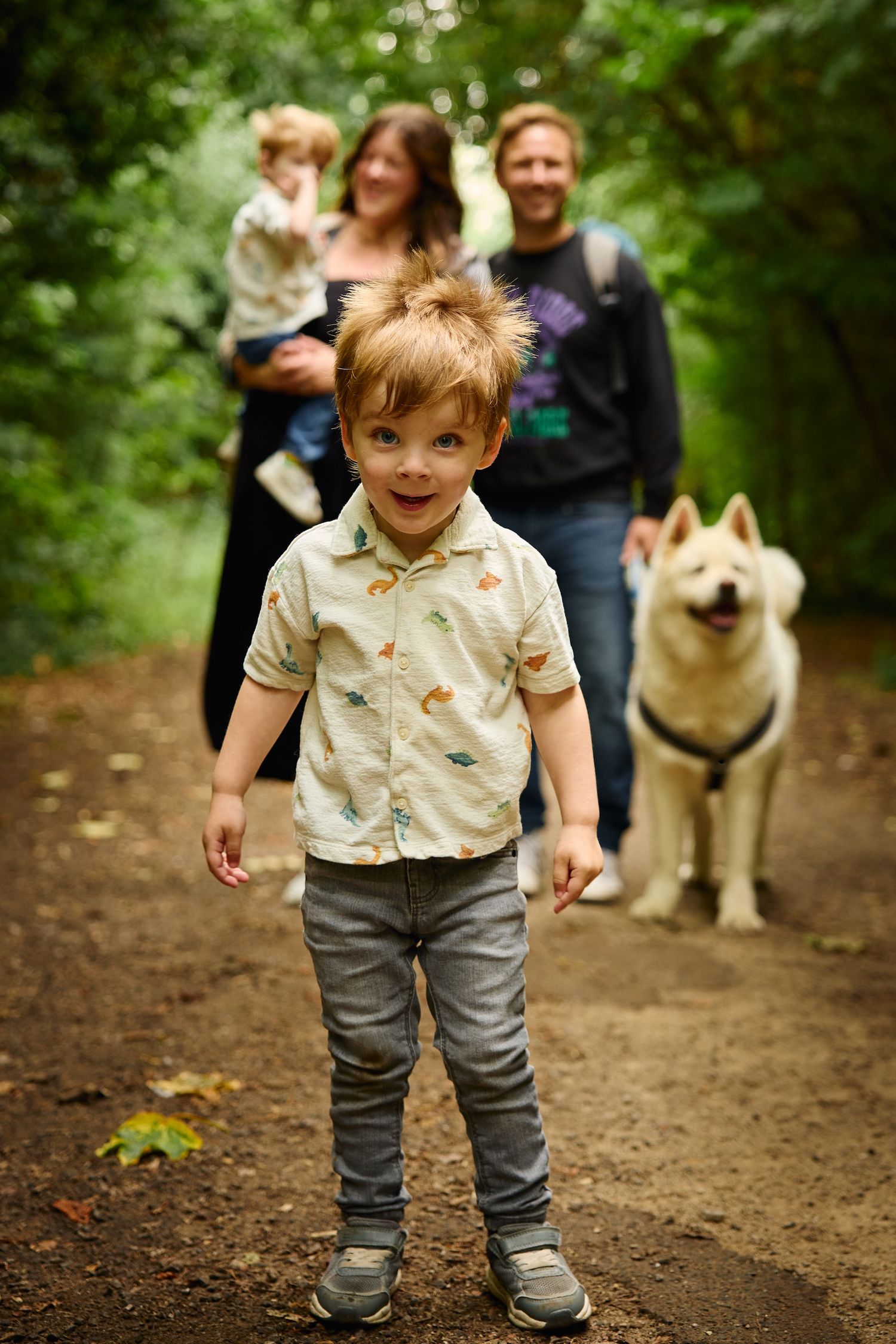 Child walking on dirt path with family and dog following behind.
