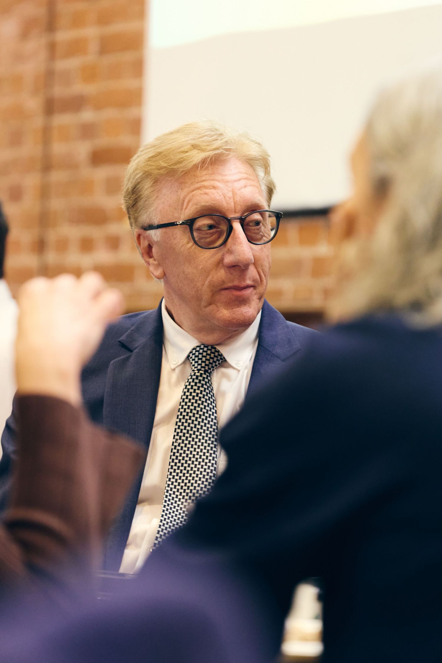 Professional man in navy suit and dotted tie listening attentively at a meeting.