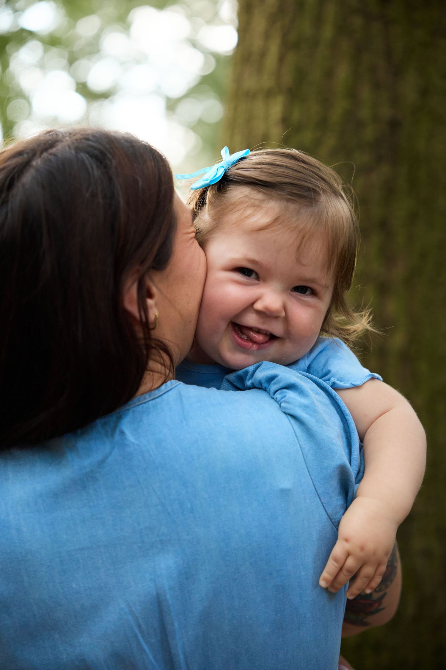 Tender moment captured between parent and child wearing matching blue outfits outdoors.