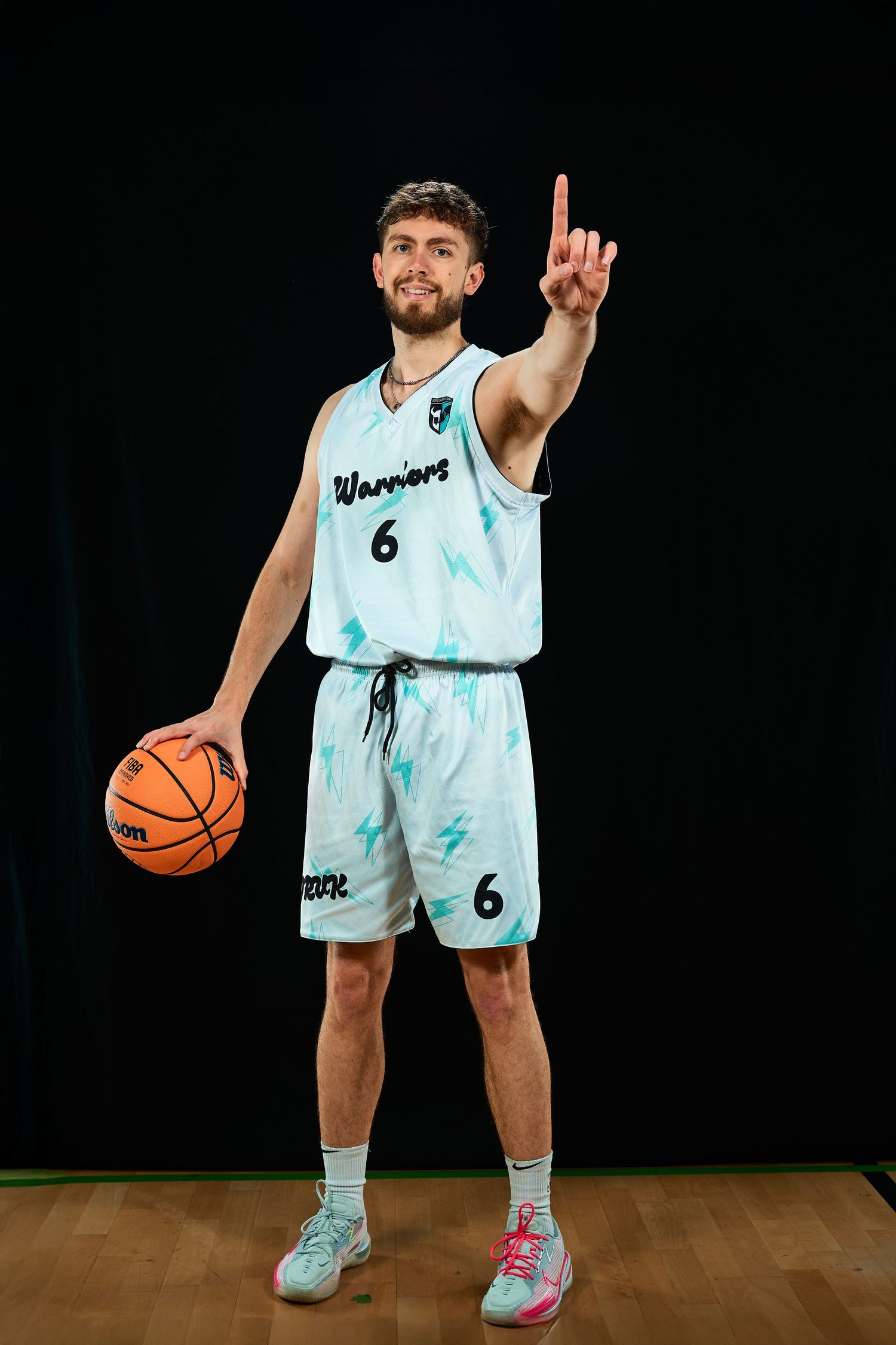 Basketball player in light blue uniform poses with ball against dark background.