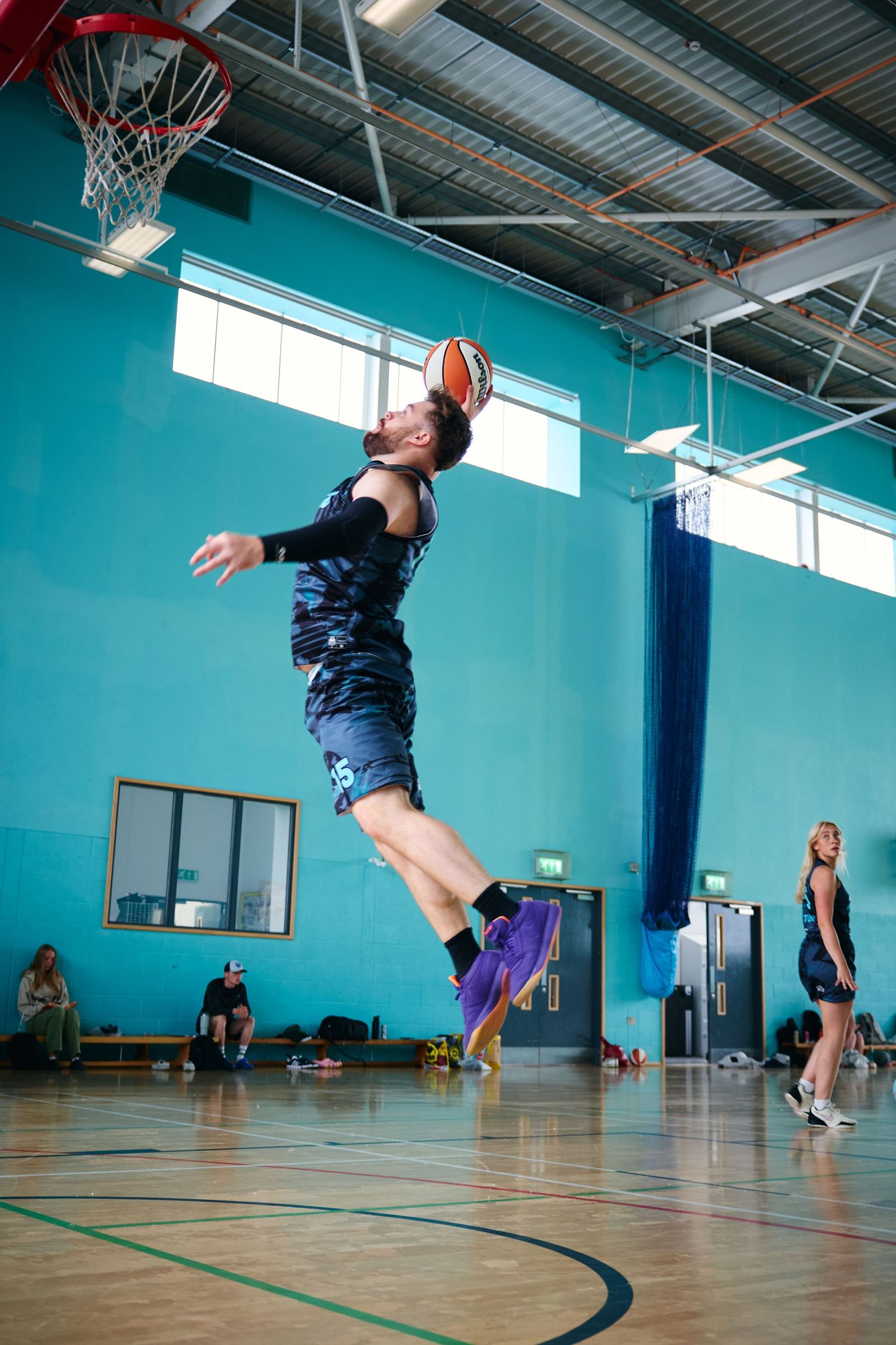 Action sequence of basketball player jumping for layup in indoor gym with blue walls.