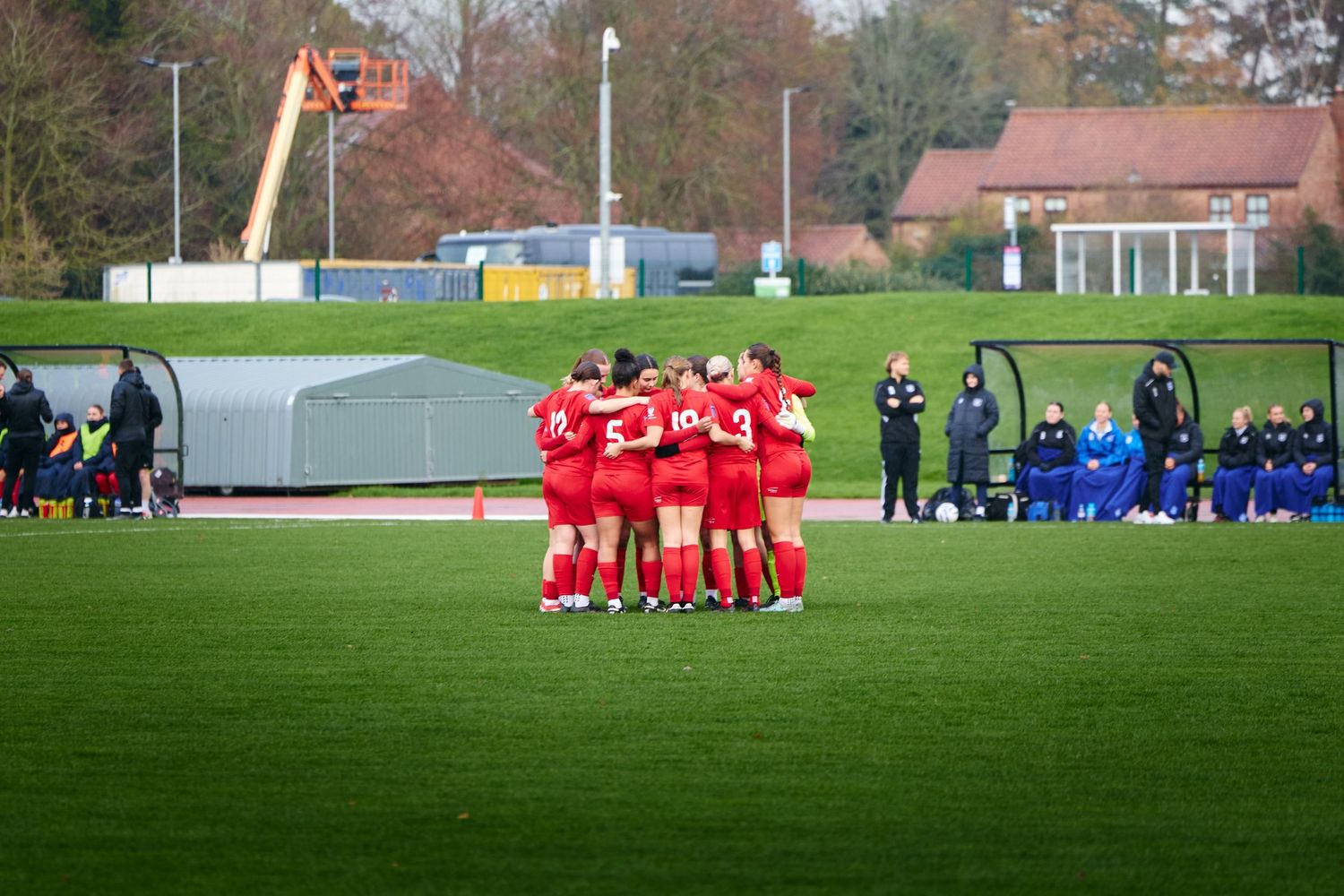 Soccer teams huddle together on opposite ends of a grass field during a match.