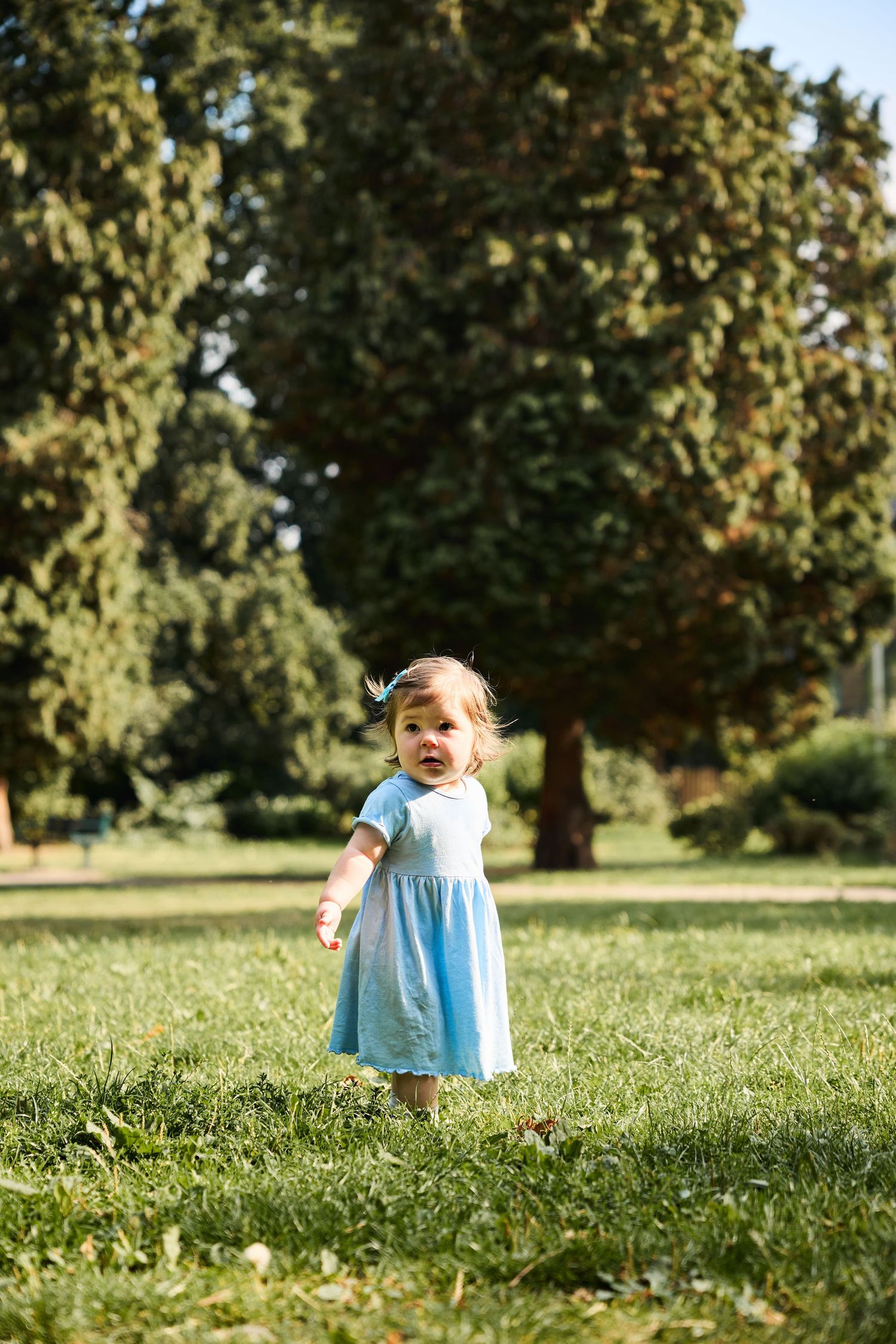 Small child in a light blue dress runs playfully through a sunny grassy field.