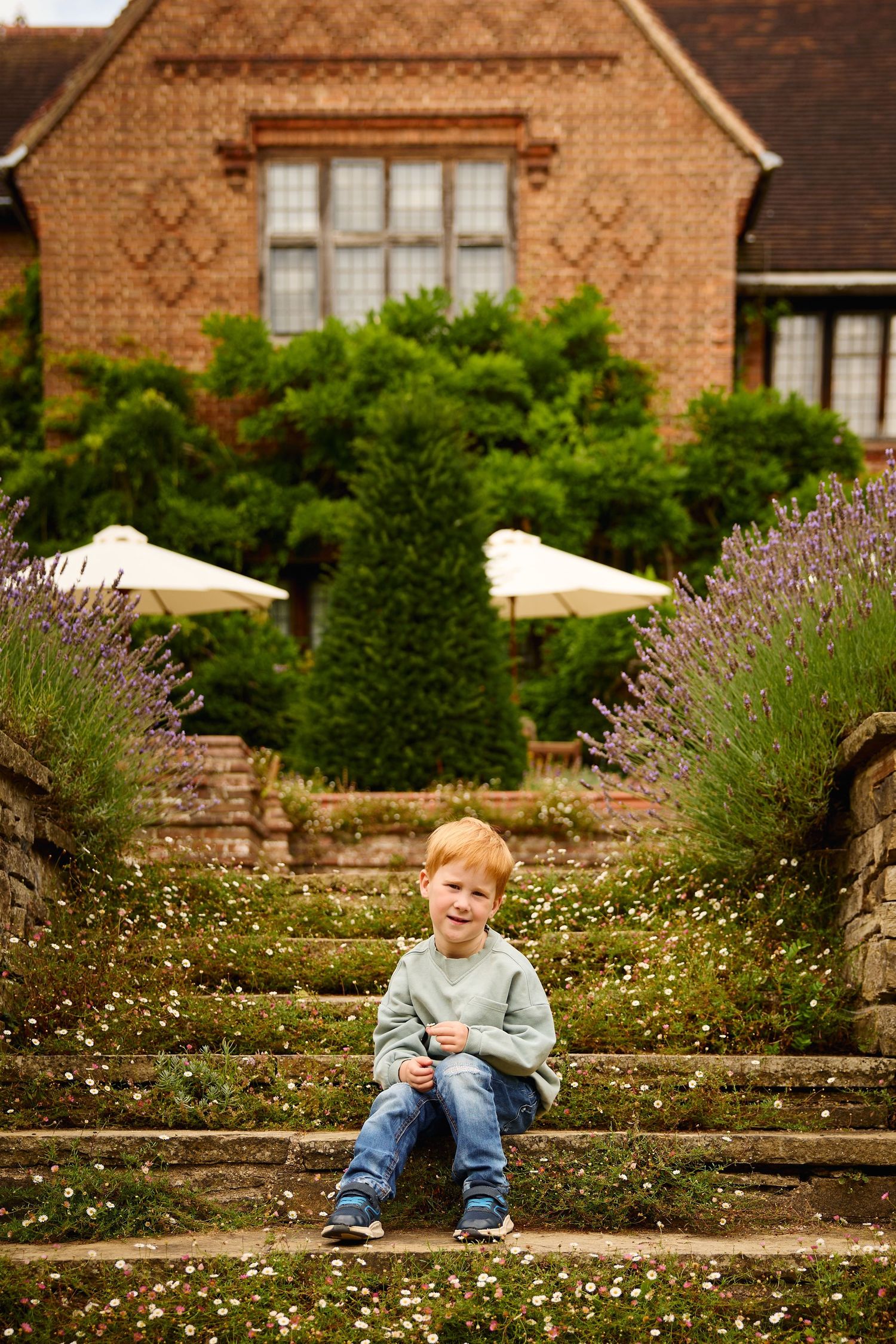 Child sitting on stone steps with brick house and lavender garden in background.