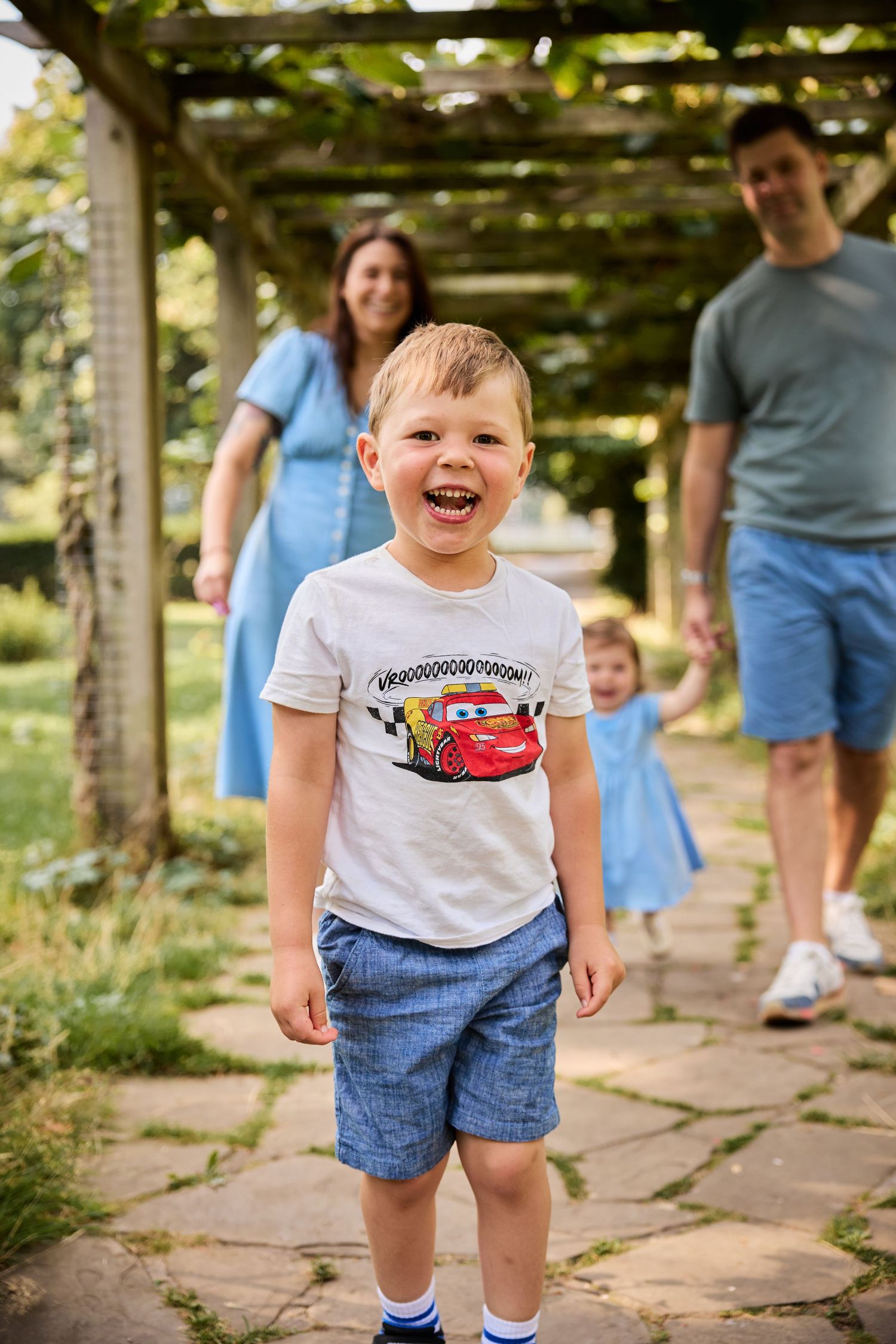 Candid family moments captured under wooden garden pergola with climbing vines.