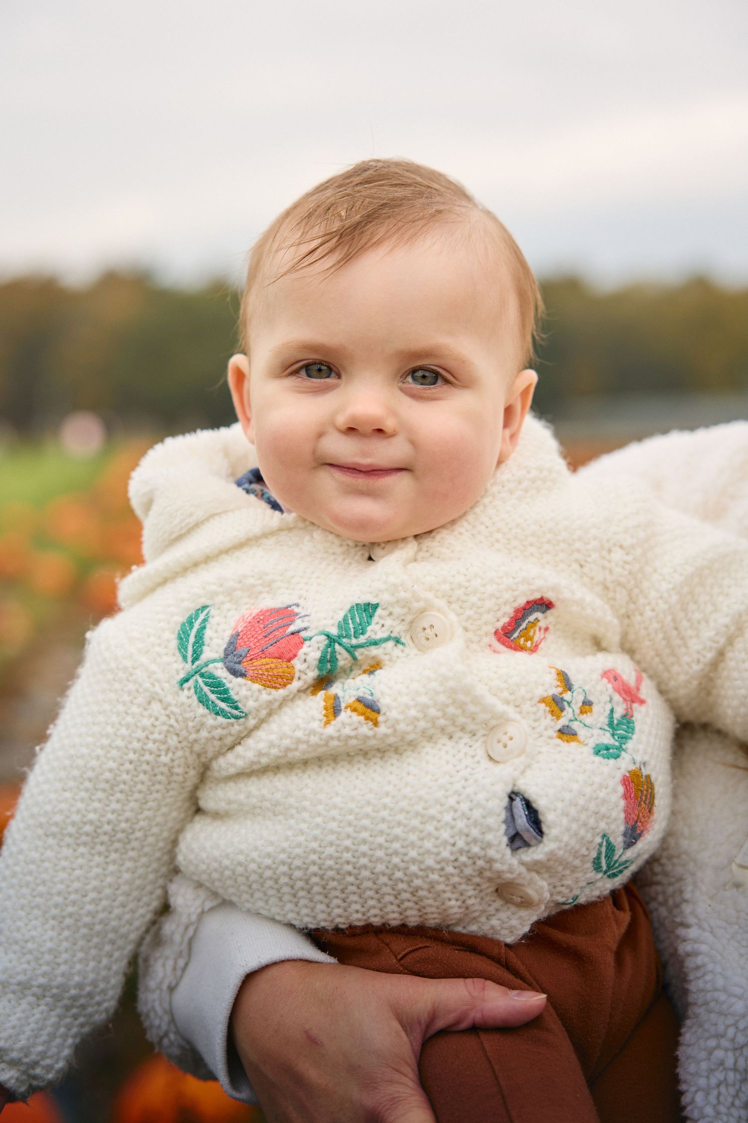 Close-up of baby wearing white embroidered sweater during fall photoshoot.