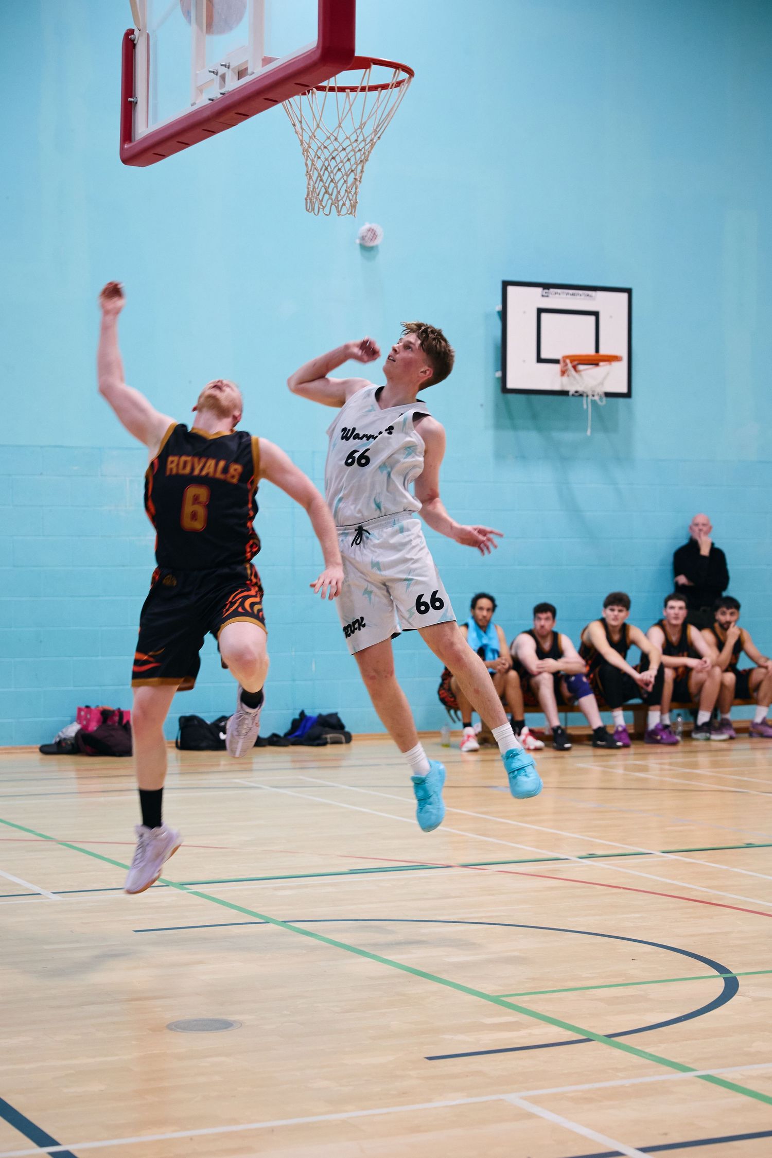 Basketball players jump for the ball during an indoor game on blue court.