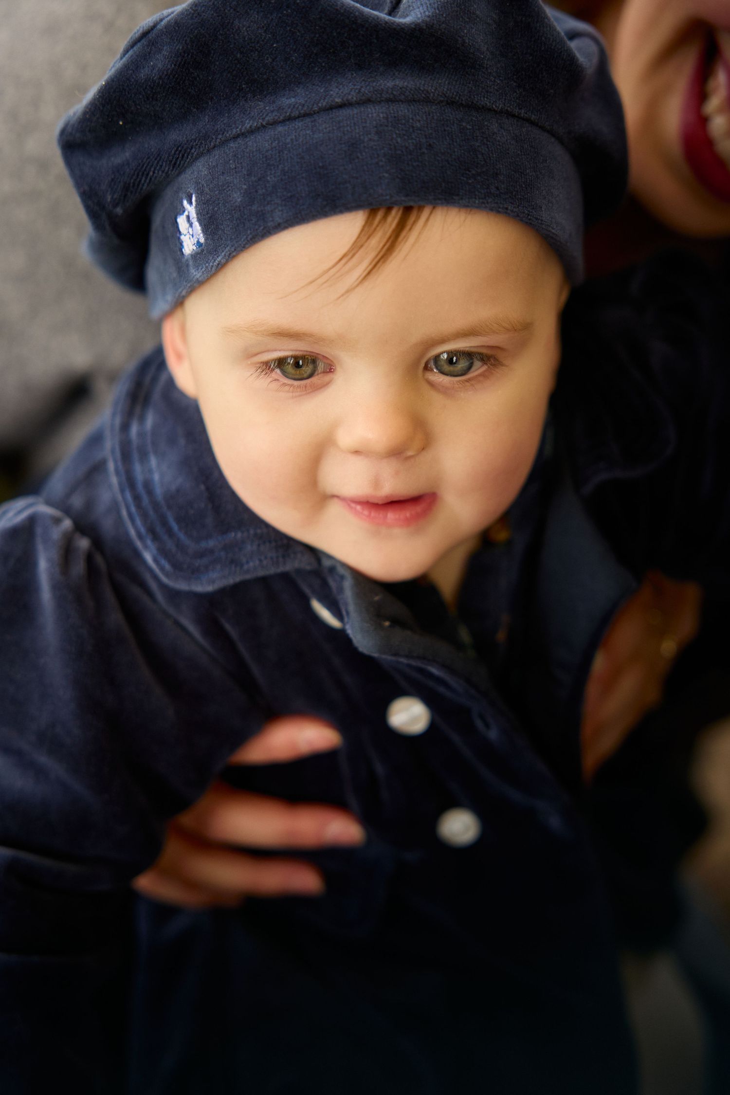 A close-up portrait of a baby wearing a navy blue hat and jacket.