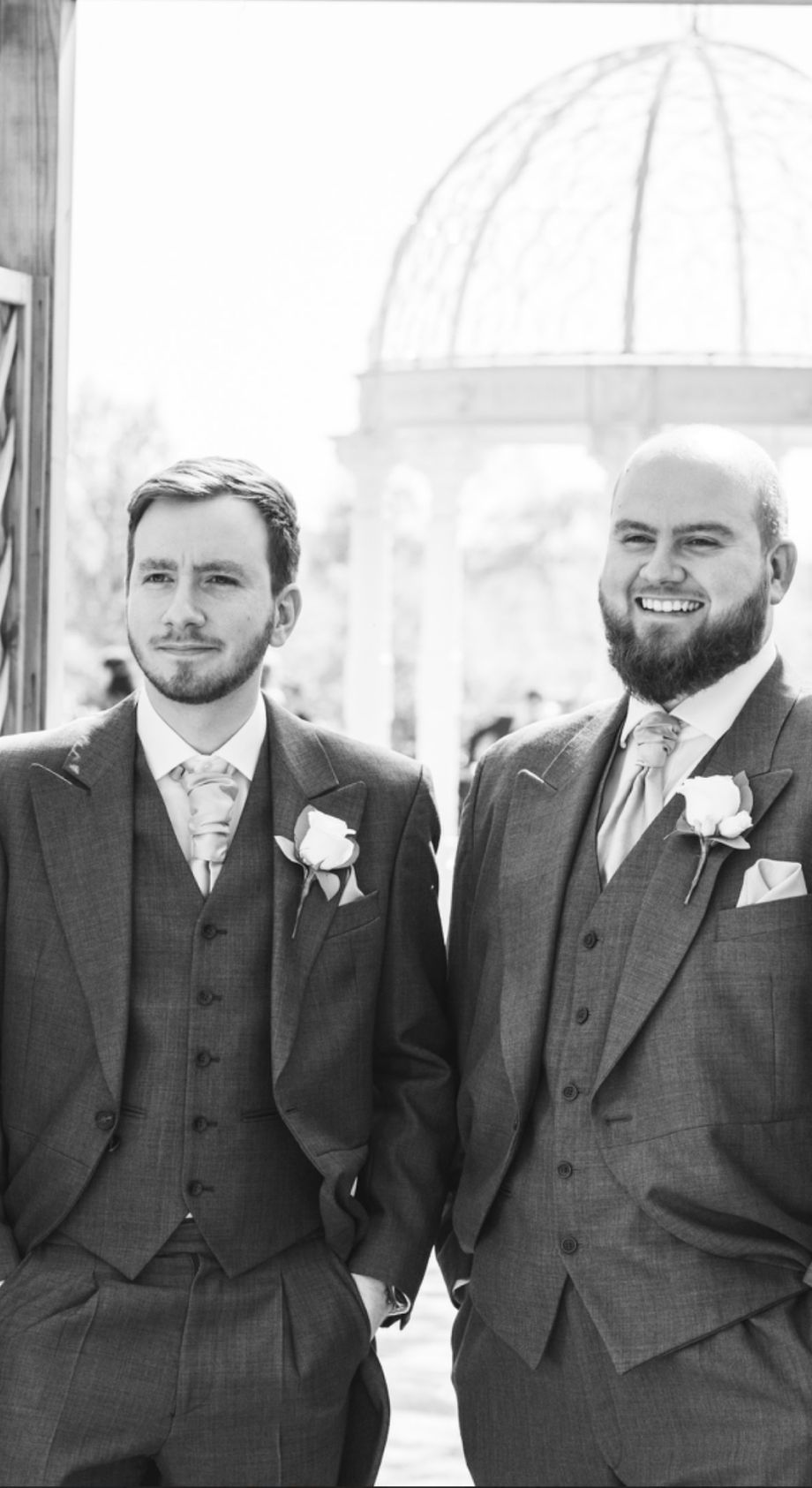 Groomsmen in matching grey suits and white boutonnieres pose together at a wedding venue.