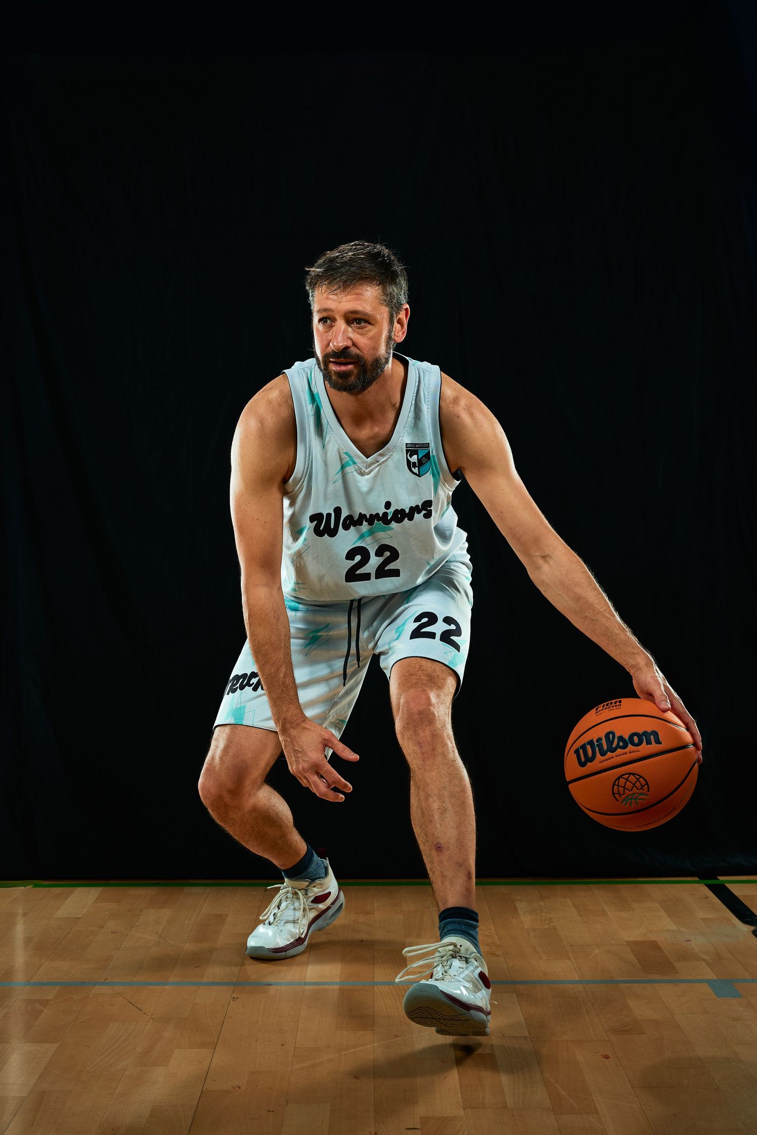 Player in light blue jersey number 22 performing crossover dribble on wooden floor.