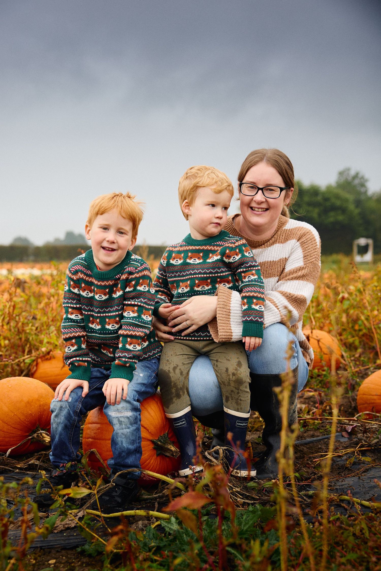 Family enjoying a fall day together in a pumpkin patch wearing coordinated sweaters.
