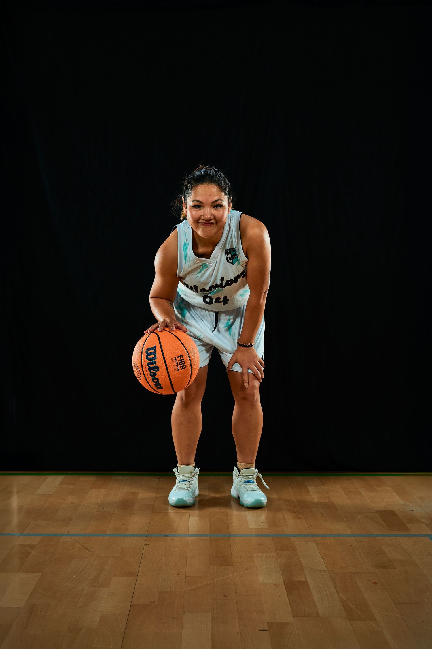 Basketball player in white uniform crouching with ball on wooden court.