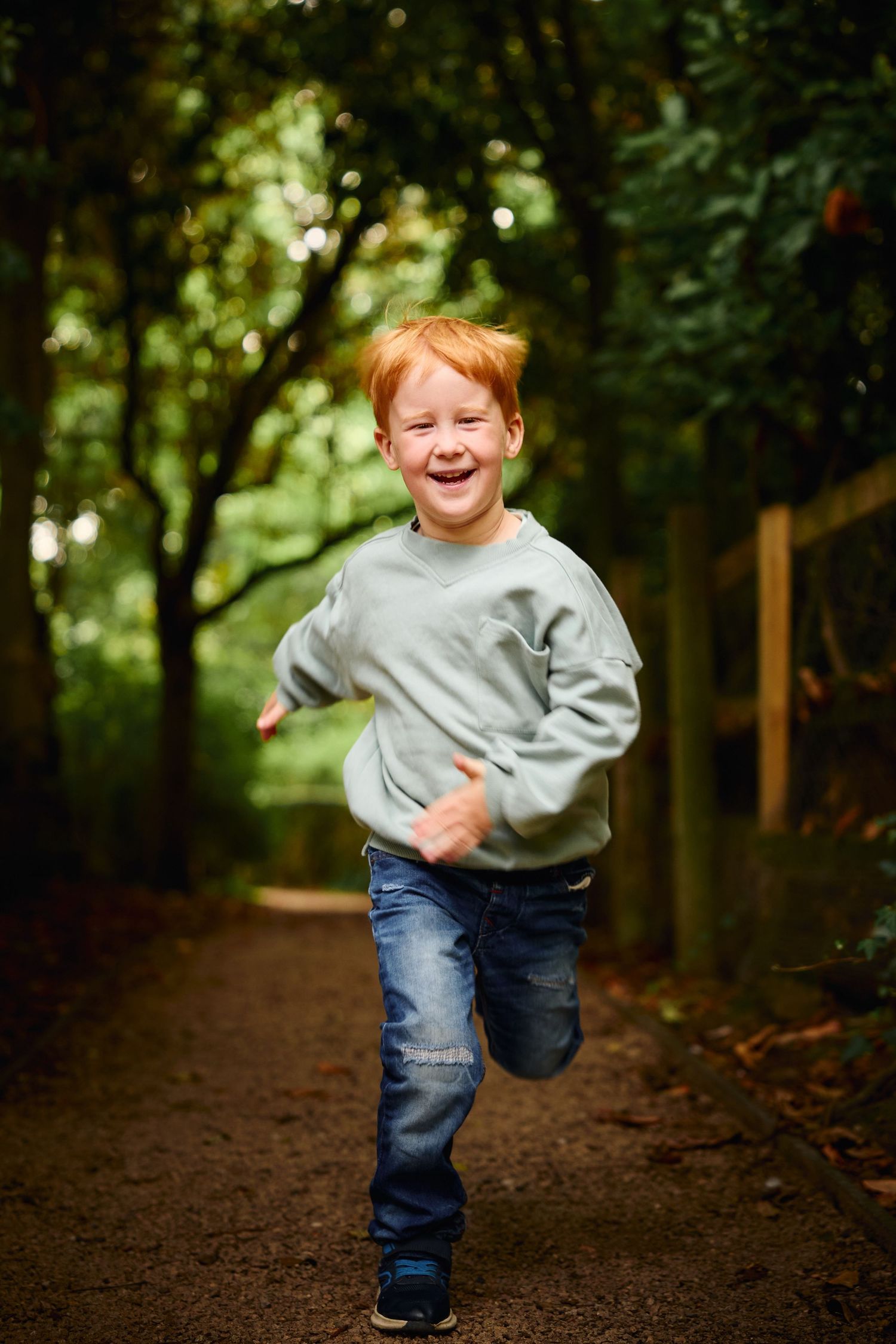 Child running playfully along a wooded path in casual attire.