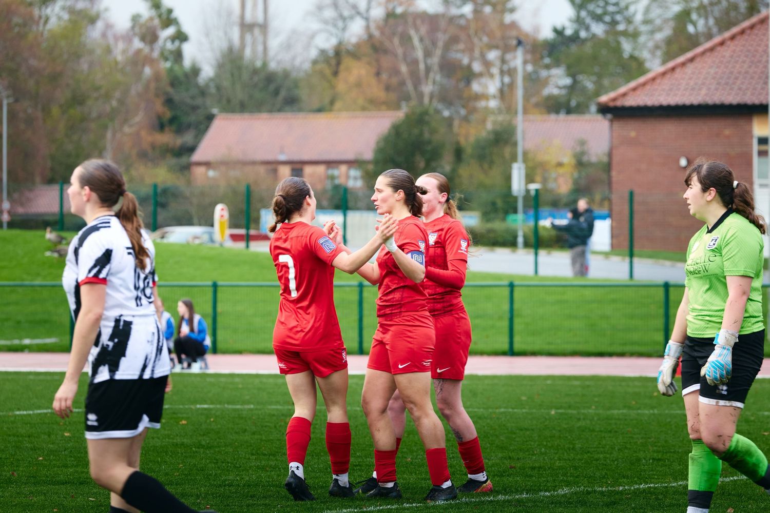 Soccer players in red and black-striped uniforms compete for the ball on a green grass field during a match.