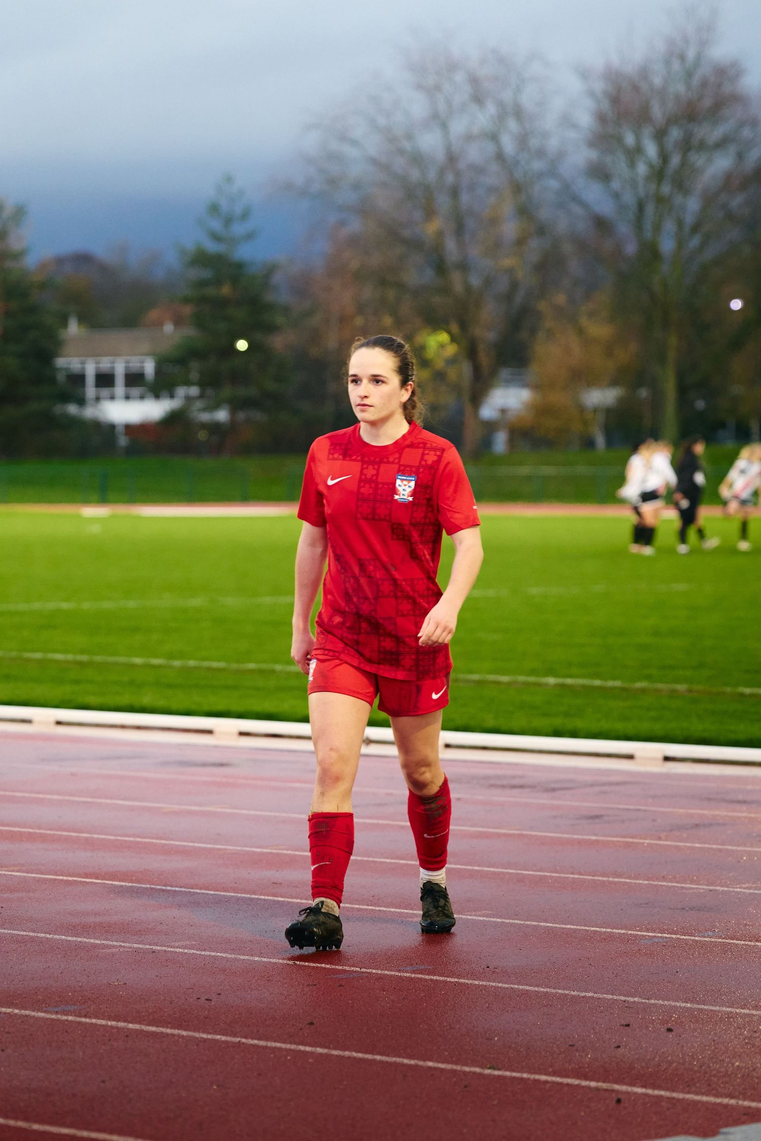 Athlete in red uniform performs dynamic stretching exercises on an outdoor running track during training session.