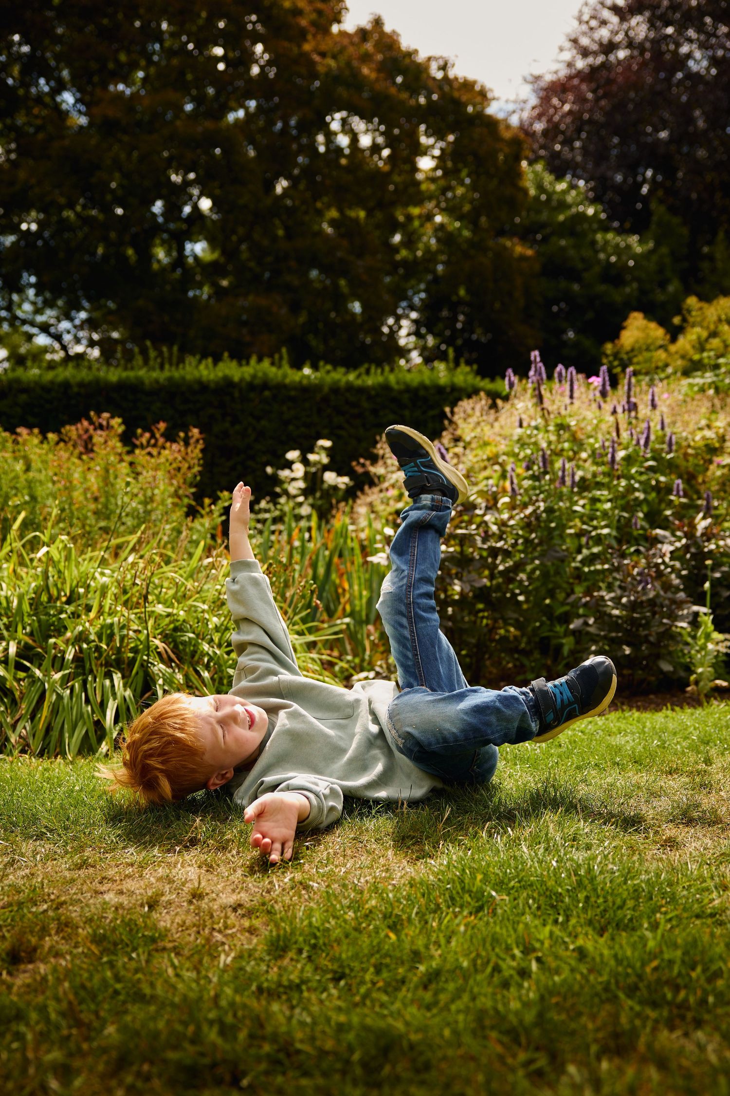 Child lying in grass surrounded by summer garden flowers.