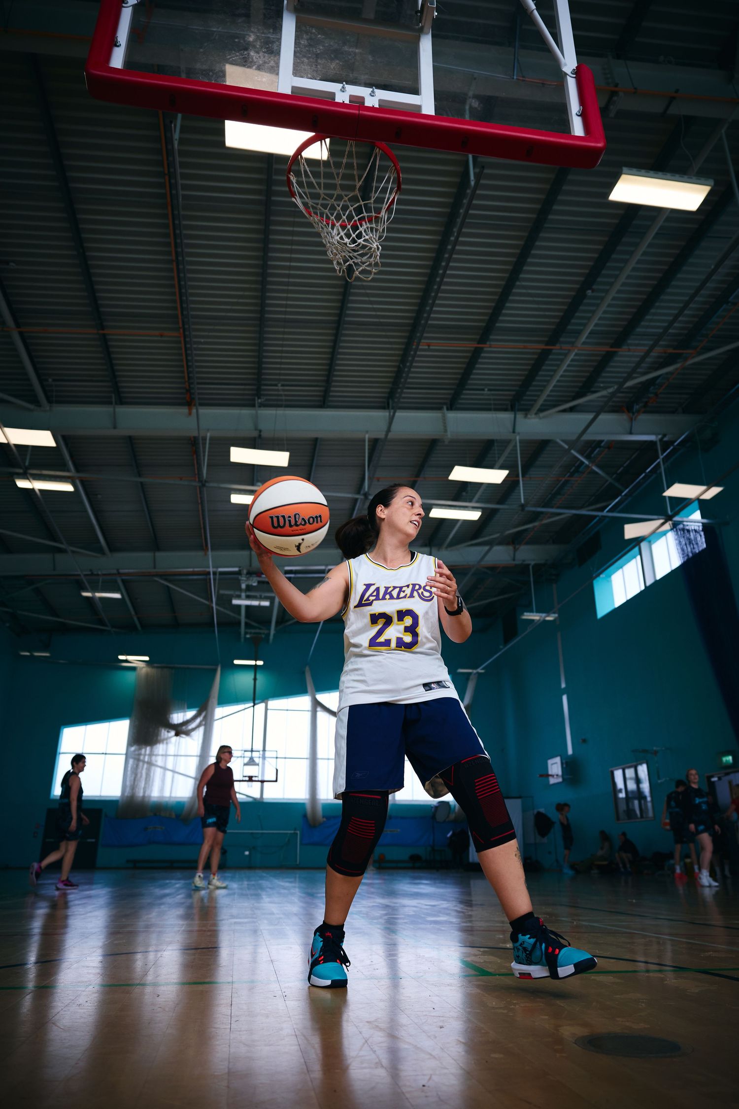 Low angle view of basketball players practicing layups in indoor gym with blue walls.