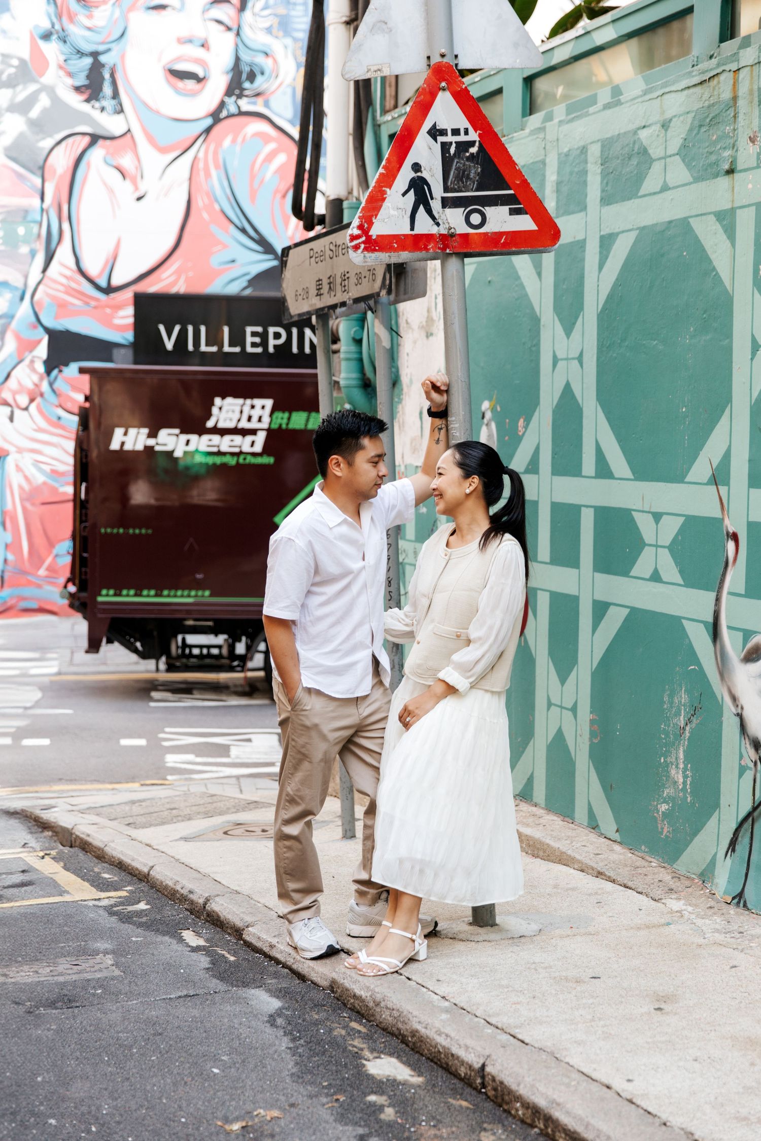 A couple shares a romantic moment on a city street corner with urban graffiti and in the background. Couple Photoshoot in Central, Hong Kong