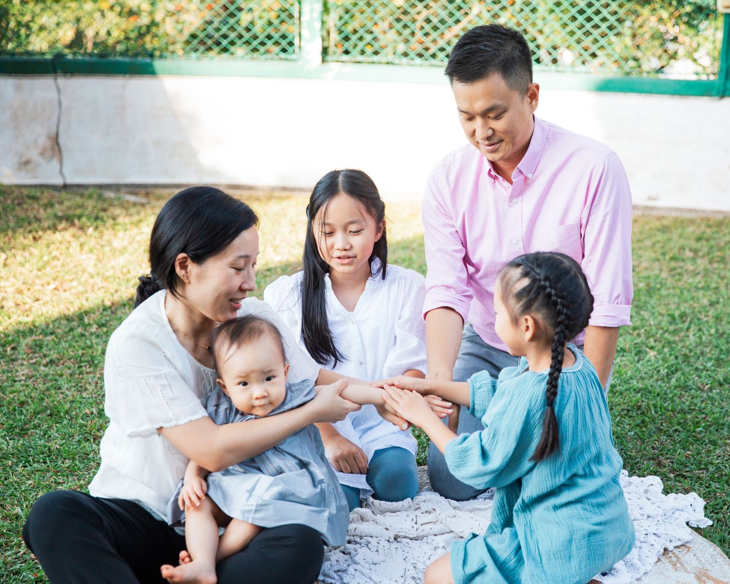 A family sits together on a blanket in a sunny garden, sharing a heartwarming moment outdoors. Family Photography in Hong Kong
