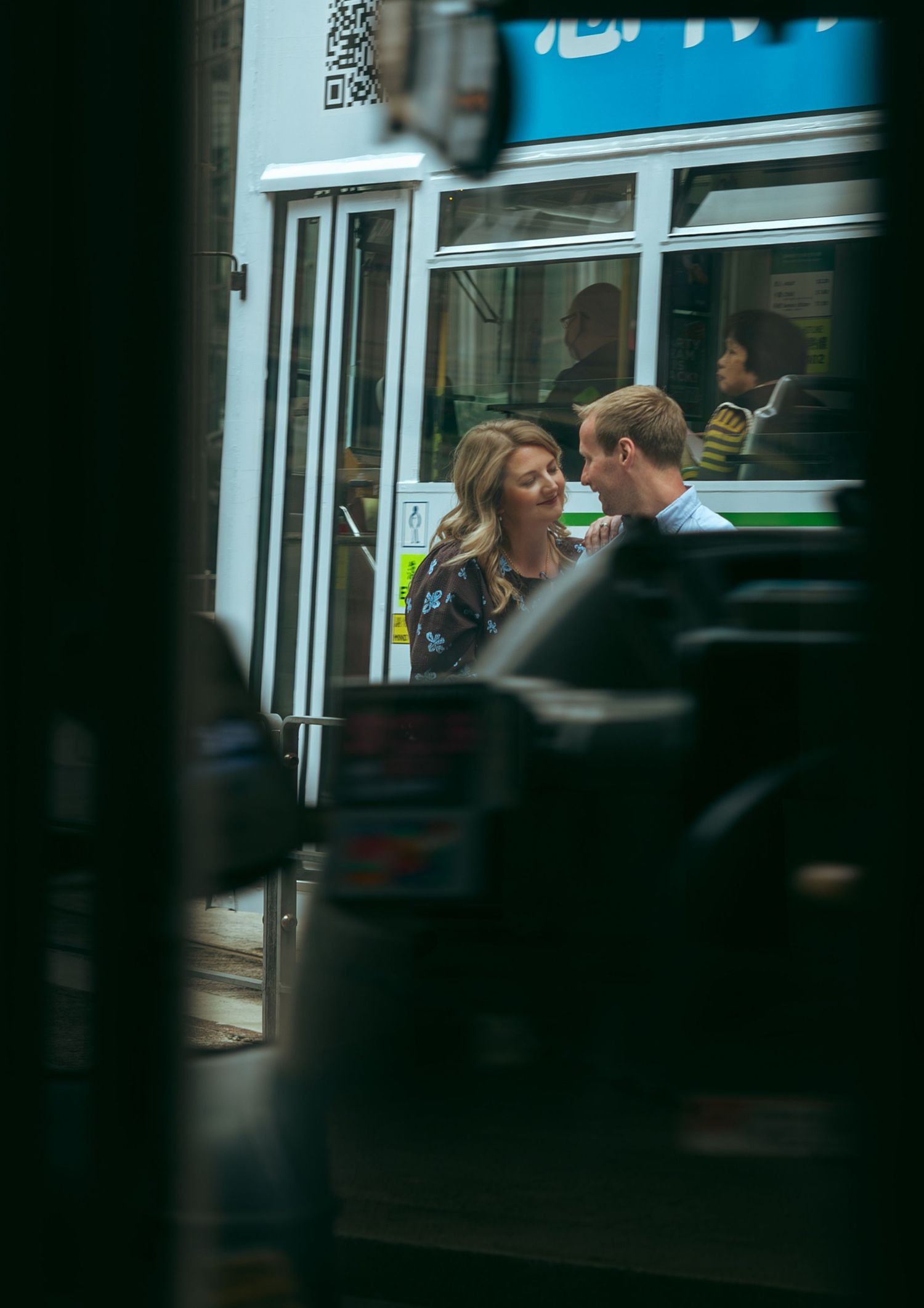 A couple shares an intimate moment outside a tram, with the woman smiling at the man in an urban setting. couple session in Hong Kong.