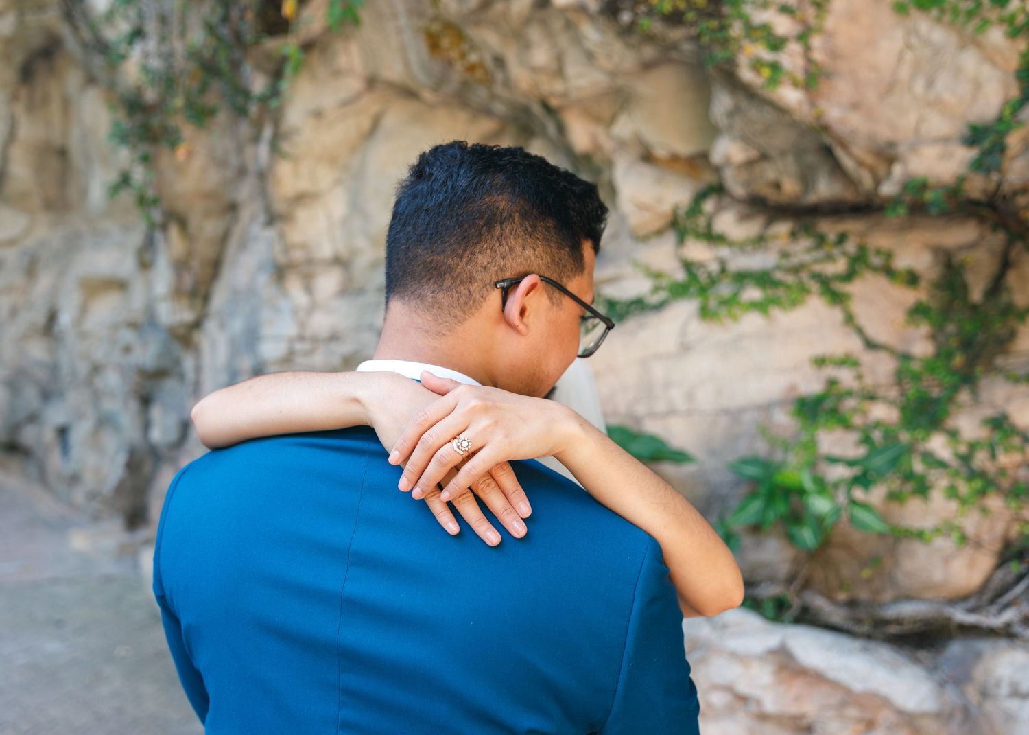 couple in blue embrace in front of a rocky wall with hanging vines and natural scenery. Civil Ceremony in Hong Kong