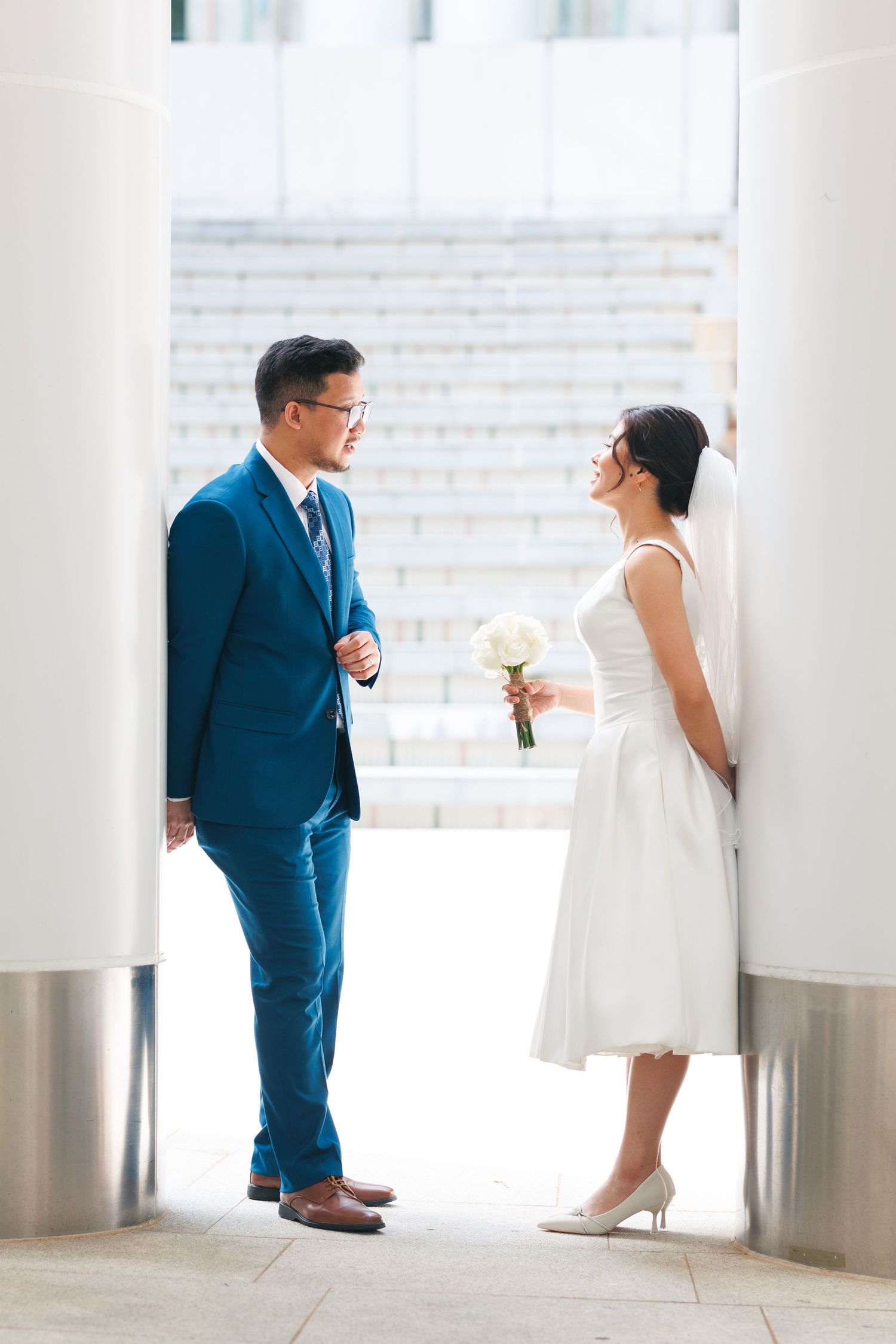 A couple in formal attire sharing a romantic moment in a bright white hallway with modern architectural elements.