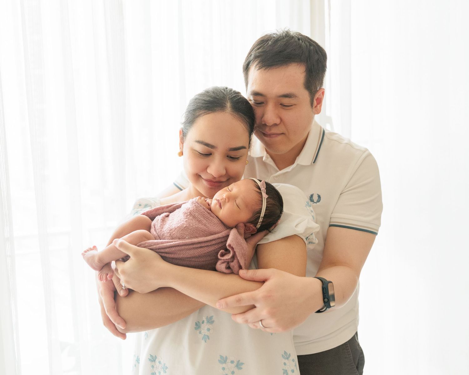Romantic couple sharing tender moment while looking at their newborn  together in bright room.  In-Home Newborn Photoshoot in Hong Kong