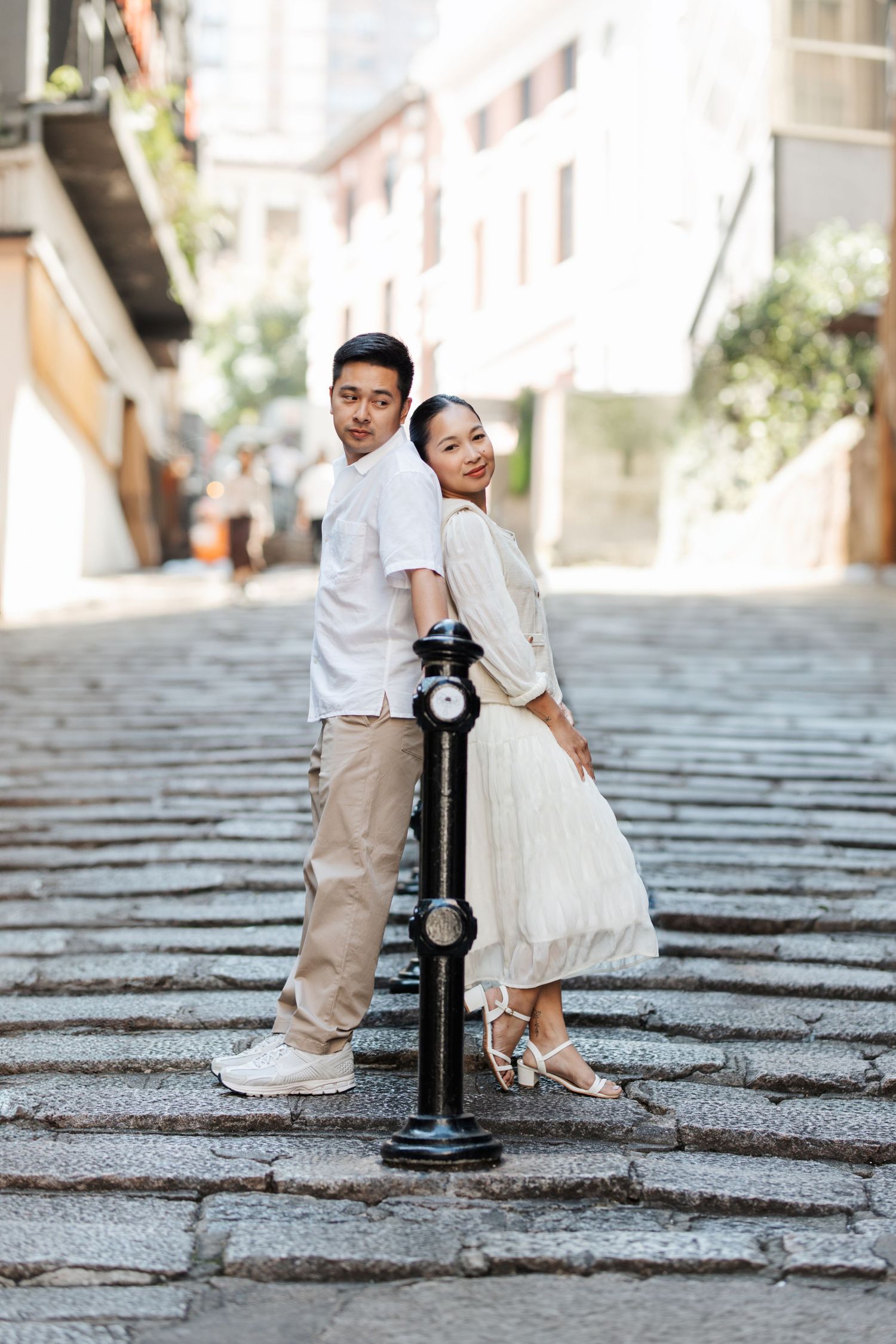 A couple in white and beige outfits poses on stone steps with a decorative black lamp post during a wedding shoot. Couple Photoshoot in HK