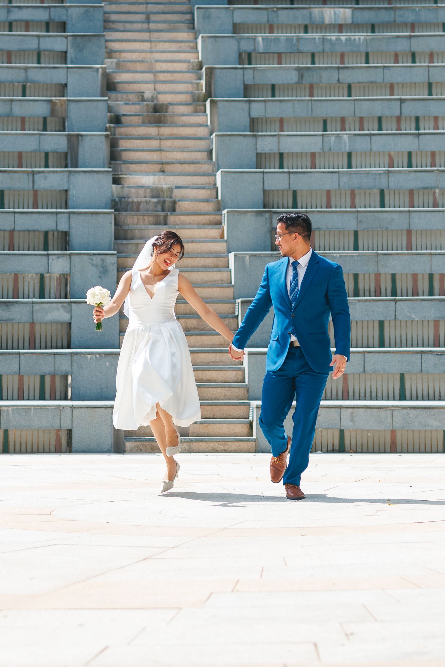 A couple in formal wedding attire performs a fun dance sequence on outdoor stairs in an urban setting. Civil Ceremony in Hong Kong