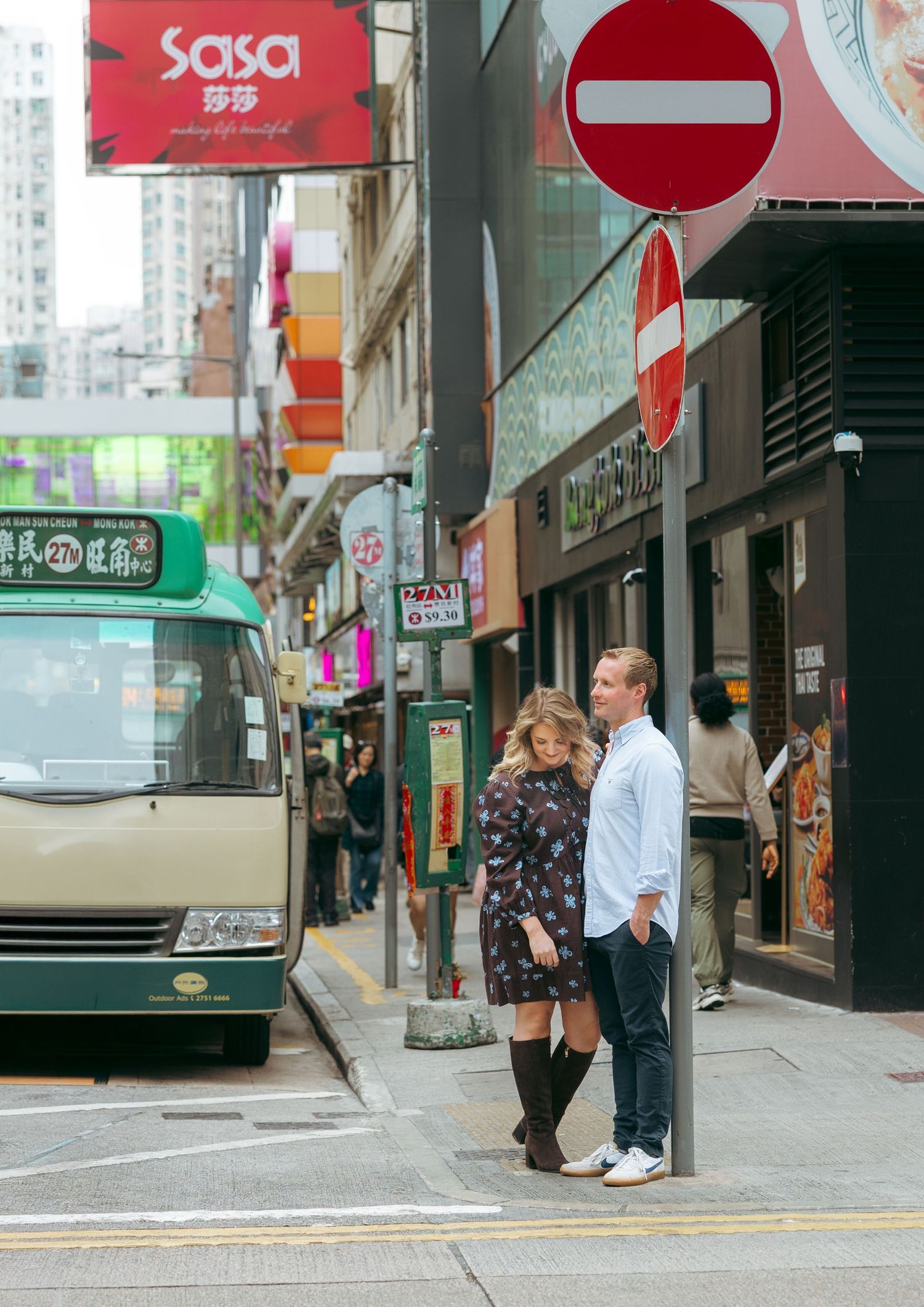 Couple standing together on a busy Hong Kong street corner near a bus stop with colorful signs couple session in Hong Kong. Pre Wedding HK