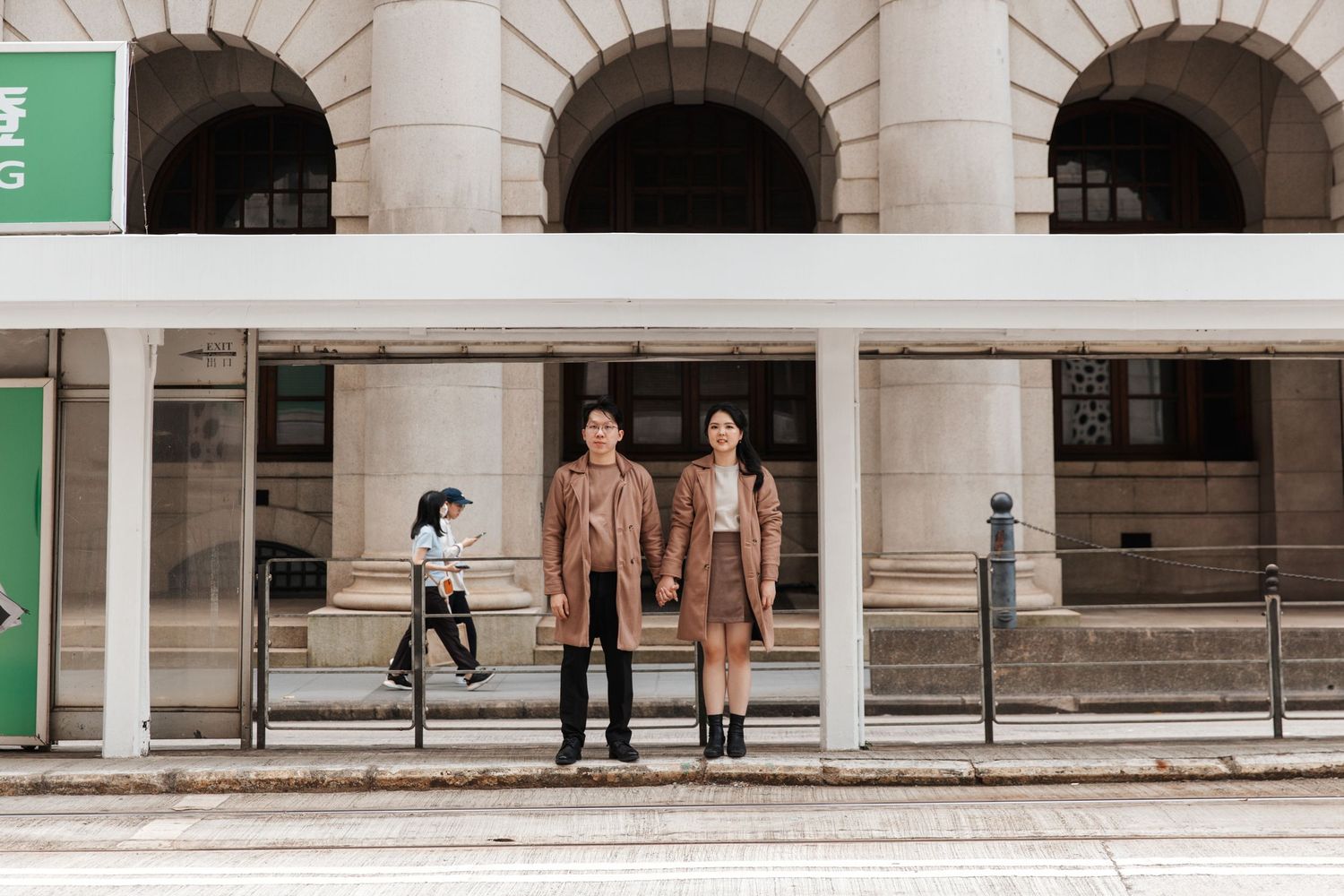 A neoclassical building with arched columns and green accents creates a dramatic architectural perspective. Couple Photoshoot in Hong Kong