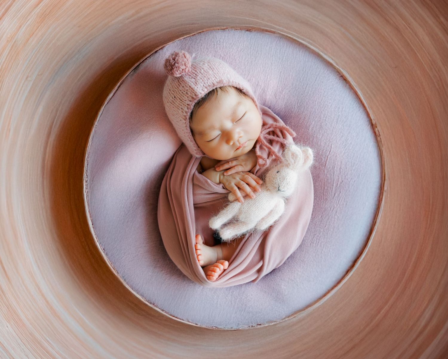 Overhead view showing a newborn baby in pink clothing lying on a curved pink bassinet in multiple artistic poses. Newborn Photography in HK